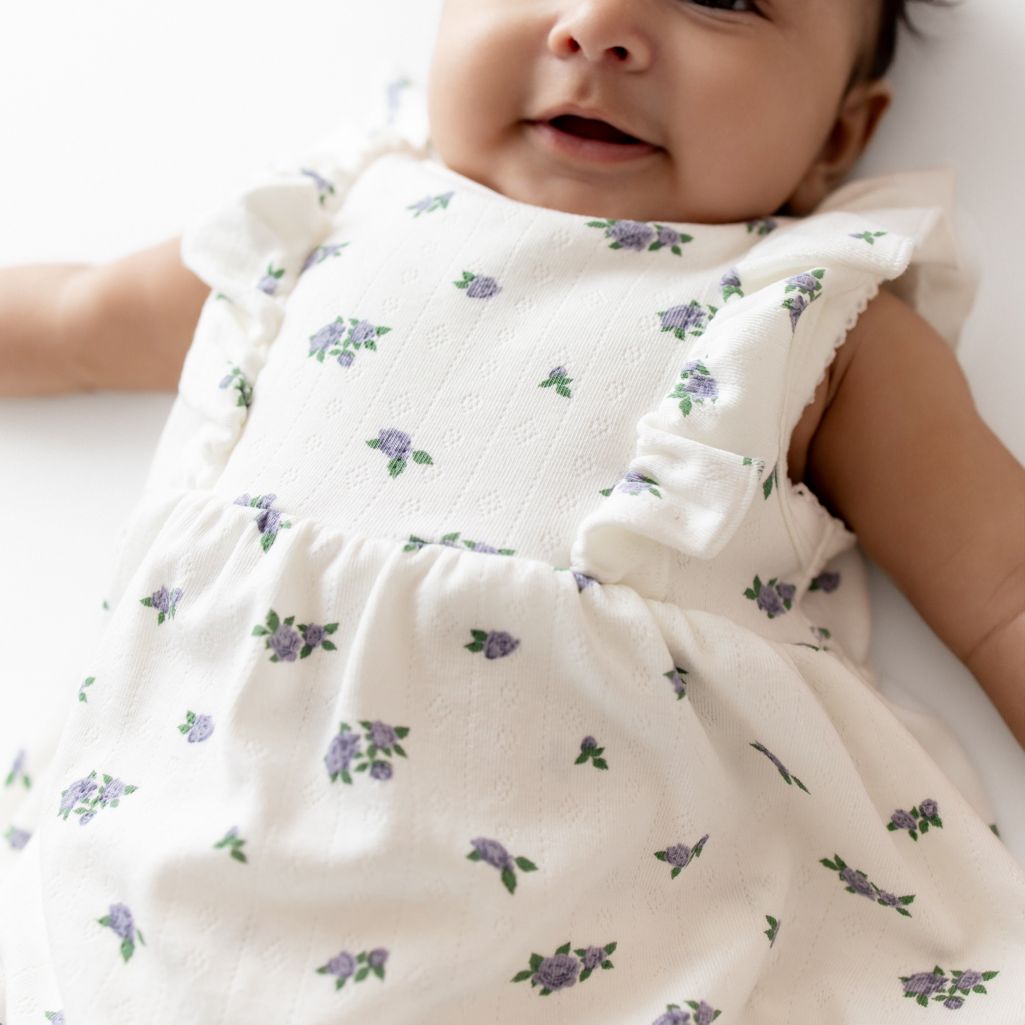 Baby wearing a white dress with purple floral patterns on a white background