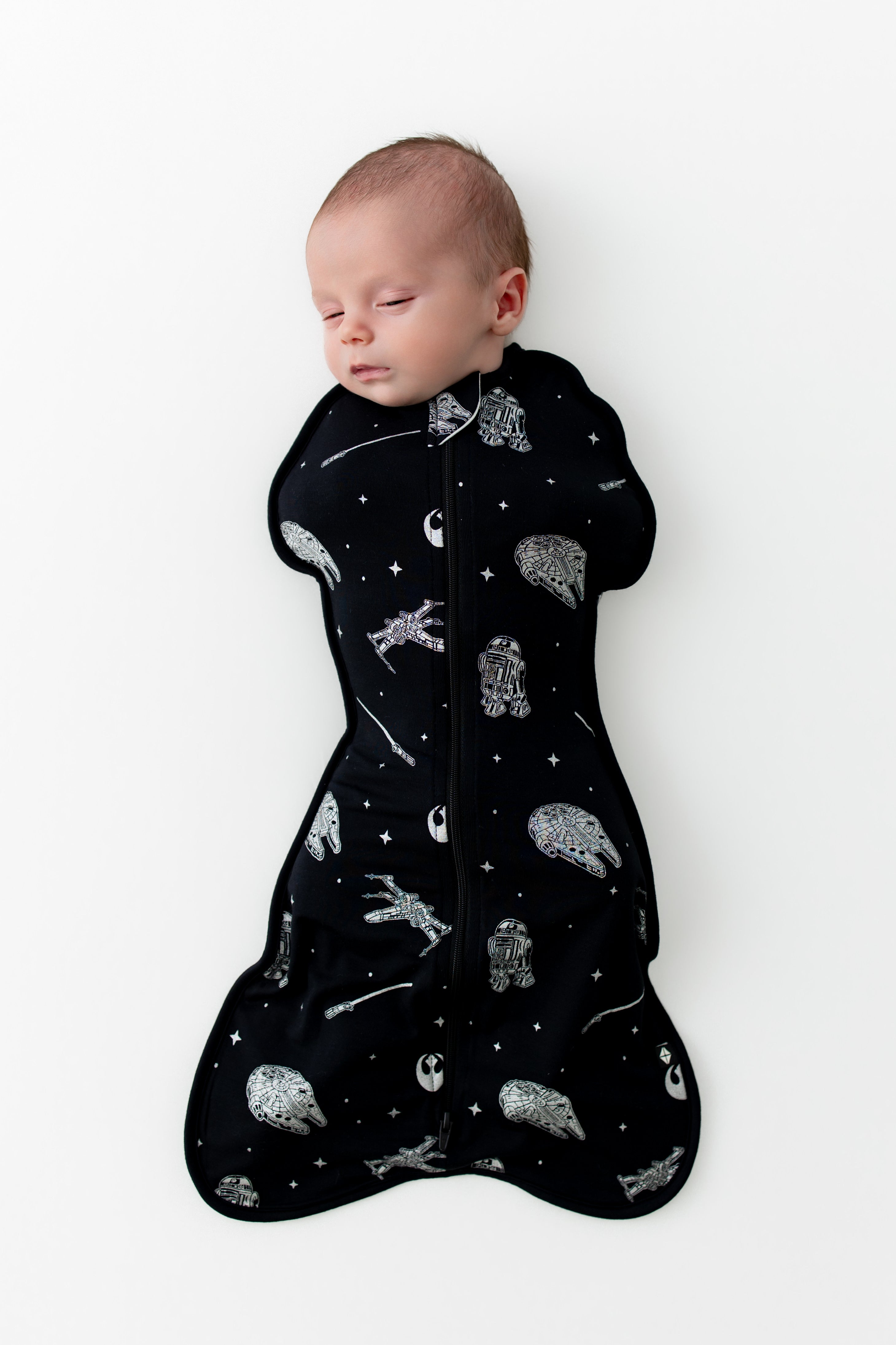 Sleeping newborn wearing the Swaddle Bag in STAR WARS™ 0.5 on a white surface