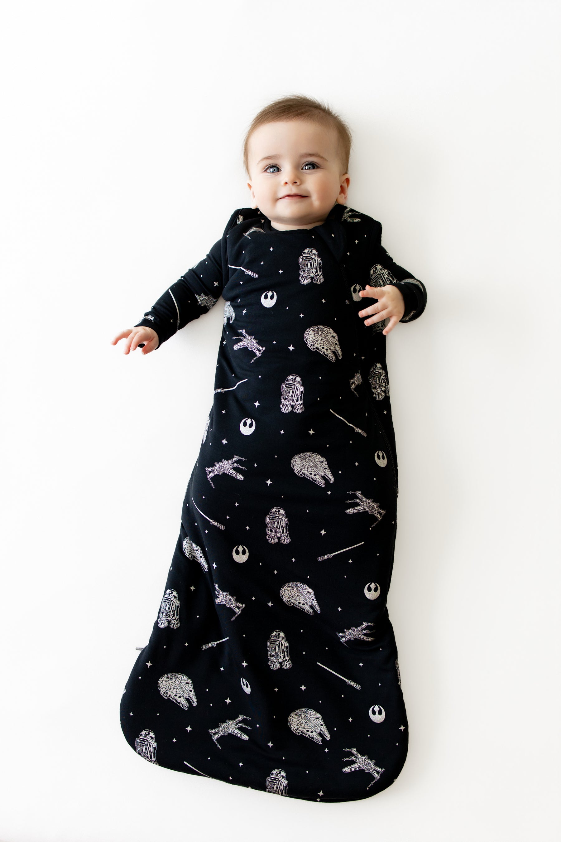 Young toddler laying on a white surface wearing the Sleep Bag in STAR WARS™ 1.0 with matching romper on underneath
