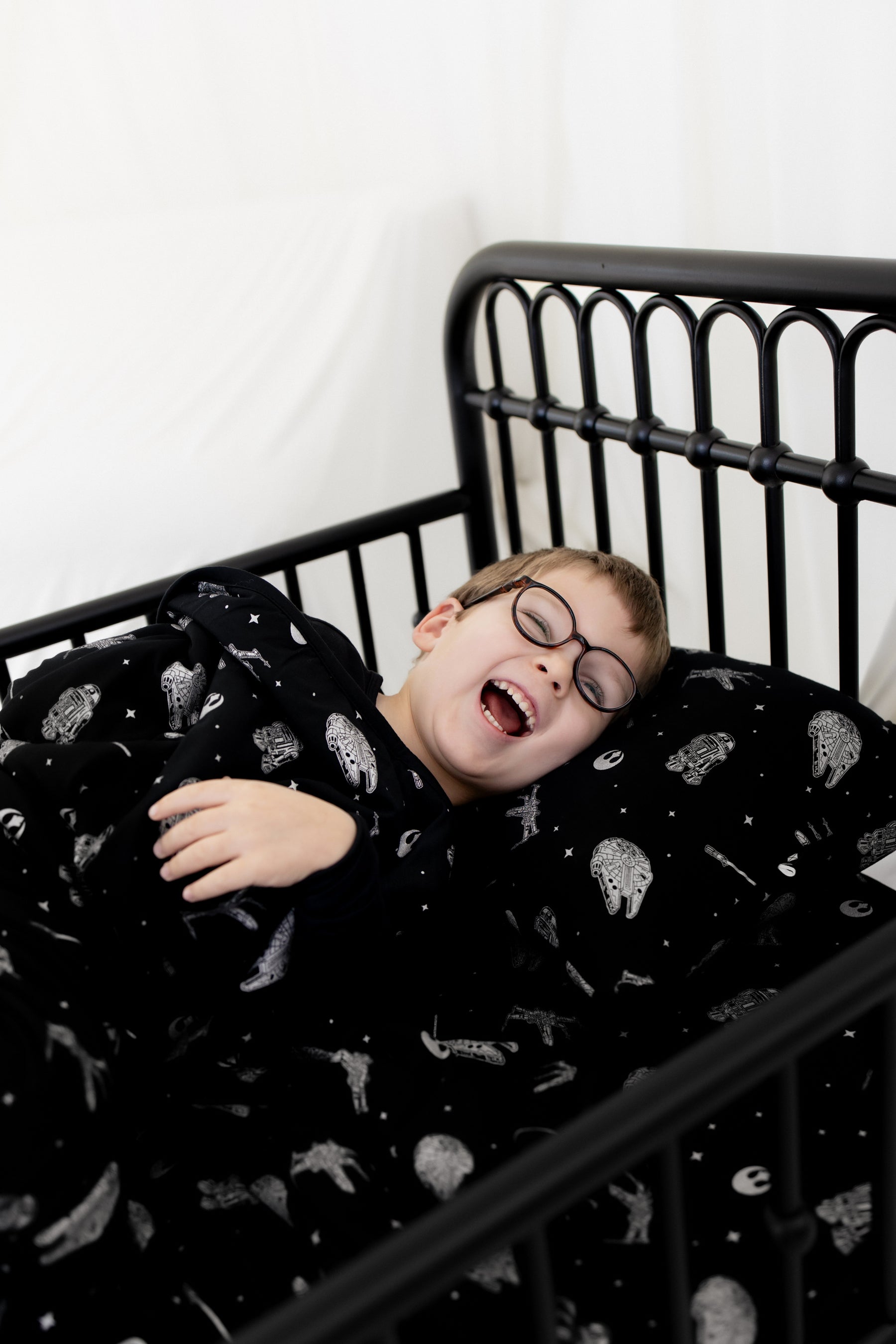 Smiling boy laying in a bed on a pillow with the Toddler Pillowcase in STAR WARS™ on it