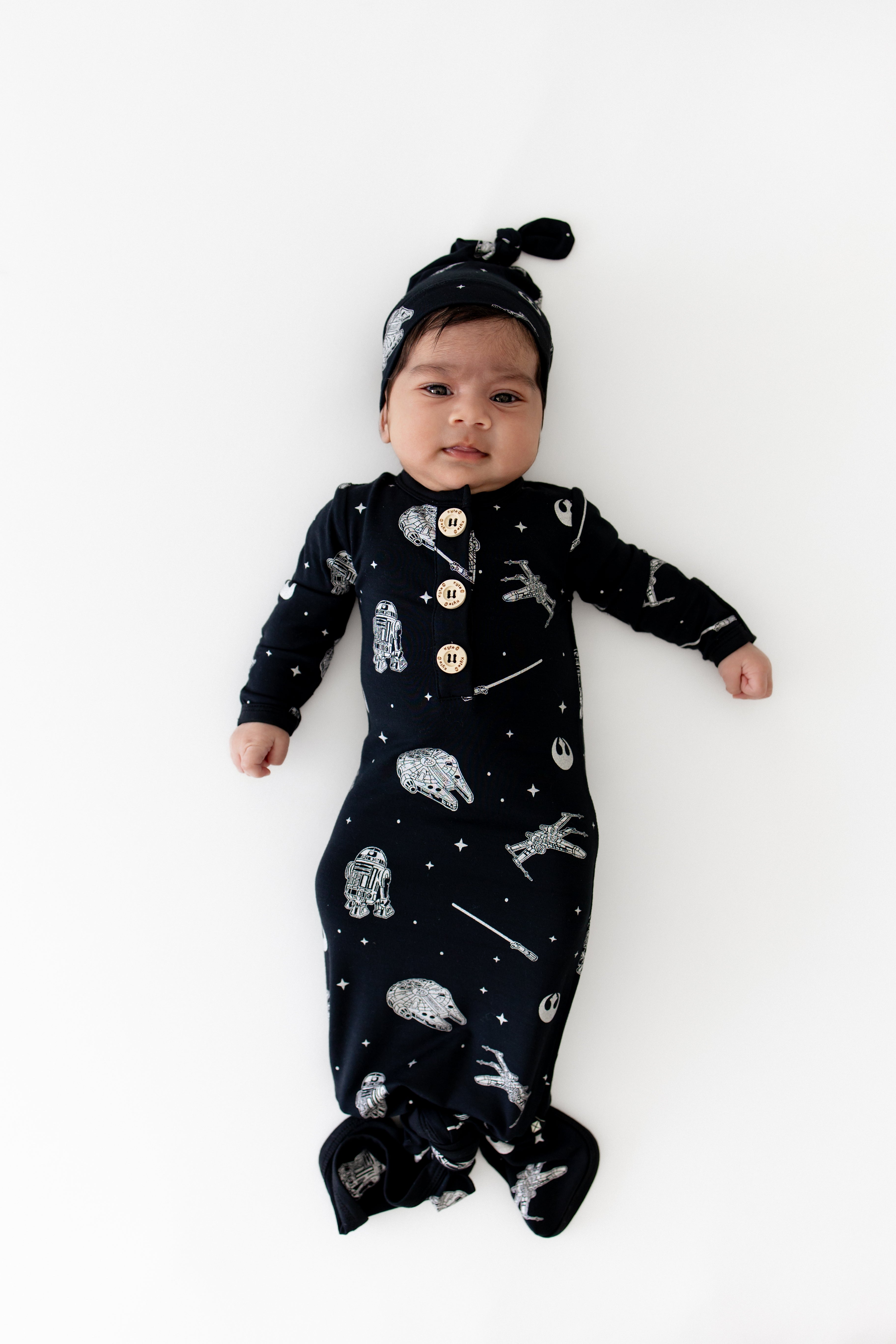 Newborn laying on a white surface wearing the Knotted Gown with Hat Set in STAR WARS™