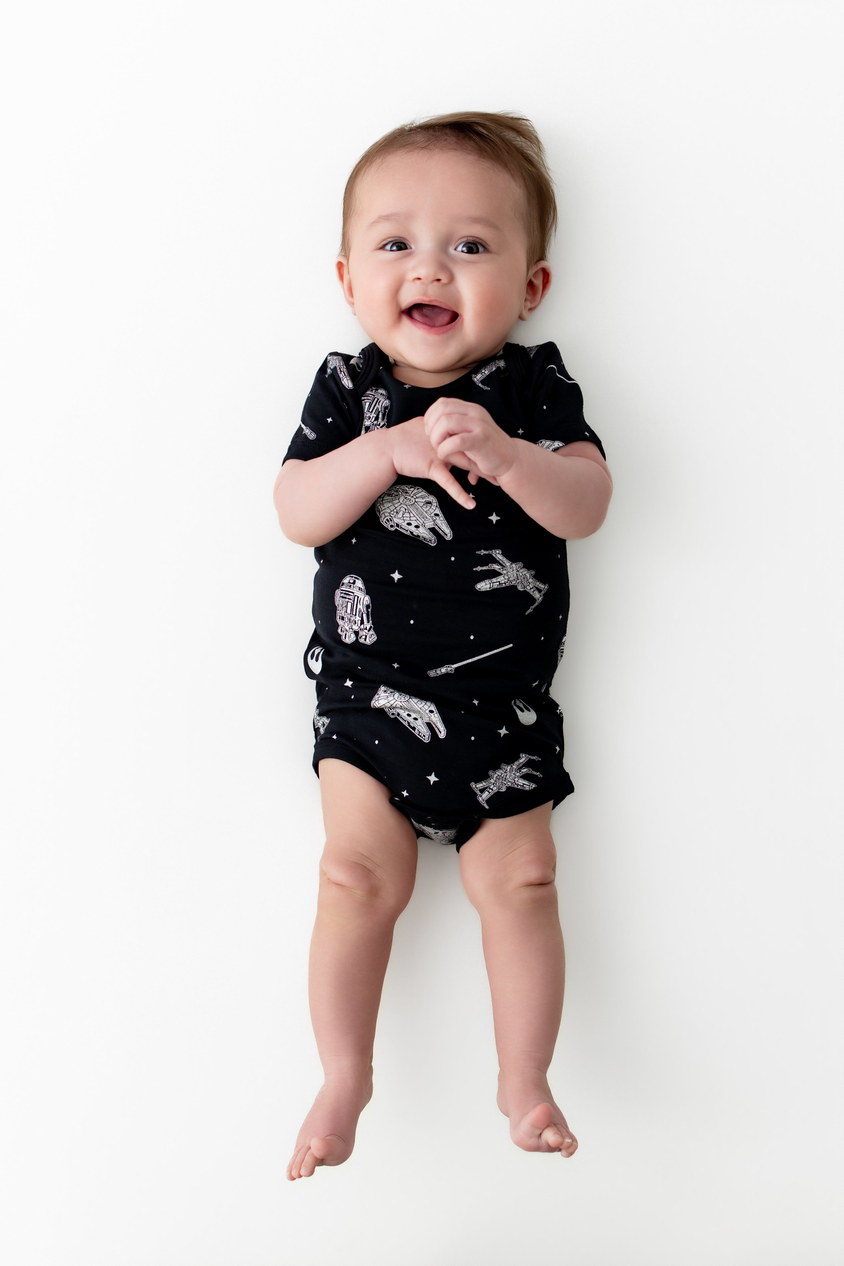 Smiling baby laying on a white surface wearing the Bodysuit in STAR WARS™