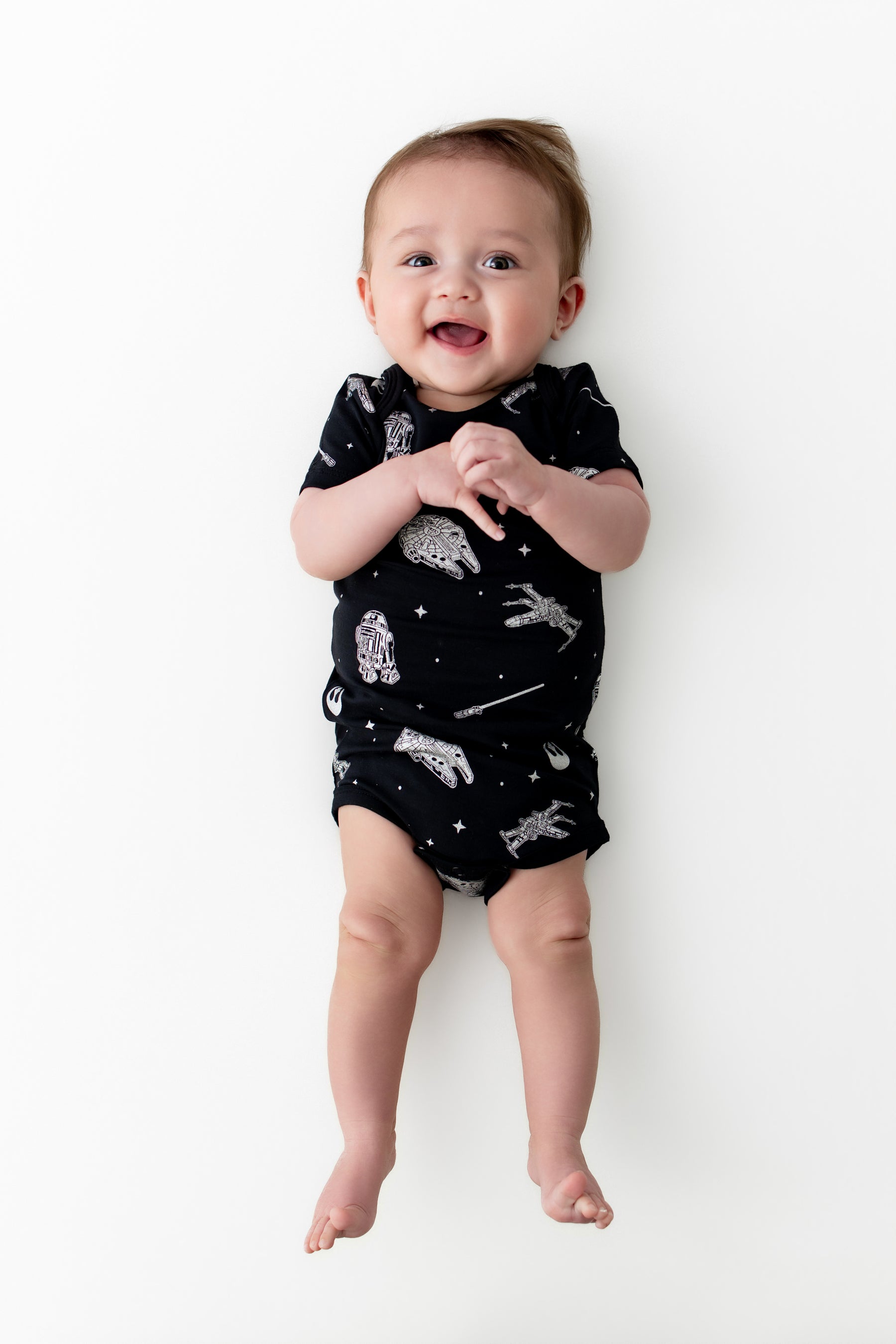 Smiling baby laying on a white surface wearing the Bodysuit in STAR WARS™
