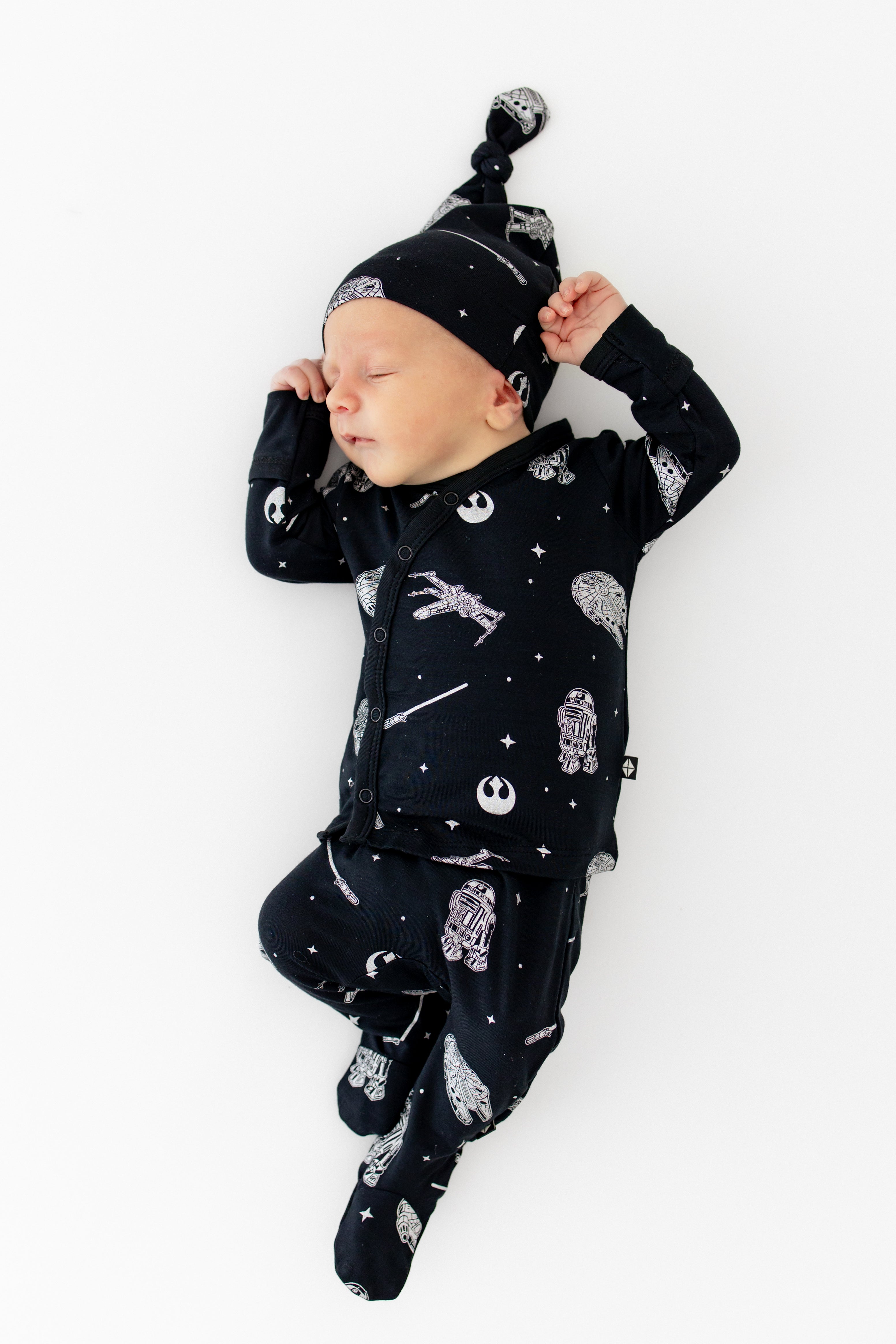 Sleeping infant stretching wearing the Take Me Home Set with Cap in STAR WARS™ laying on a white surface