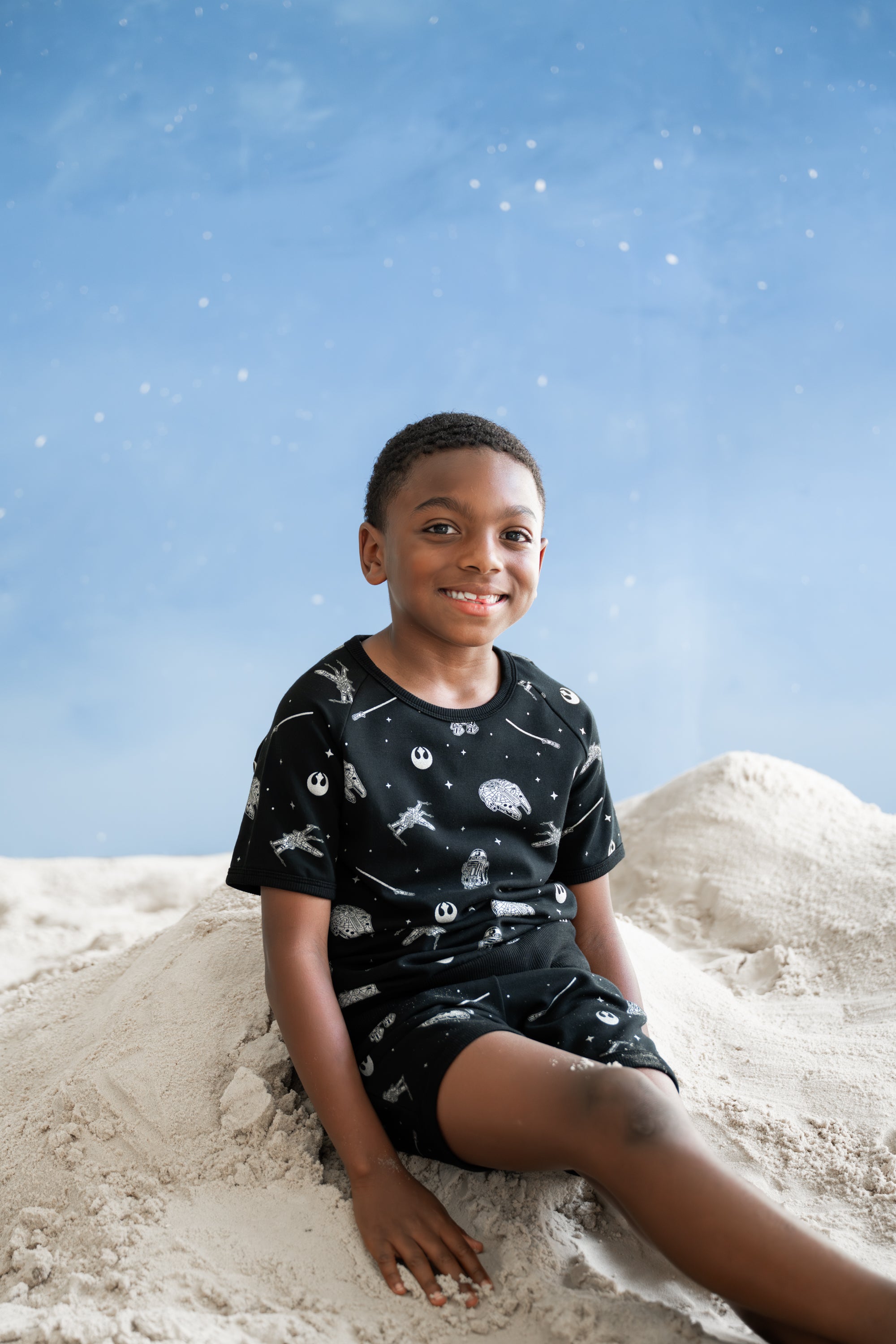 young boy sitting in the sand wearing the Short Sleeve Jogger Set in STAR WARS™ in front of a blue sky backdrop