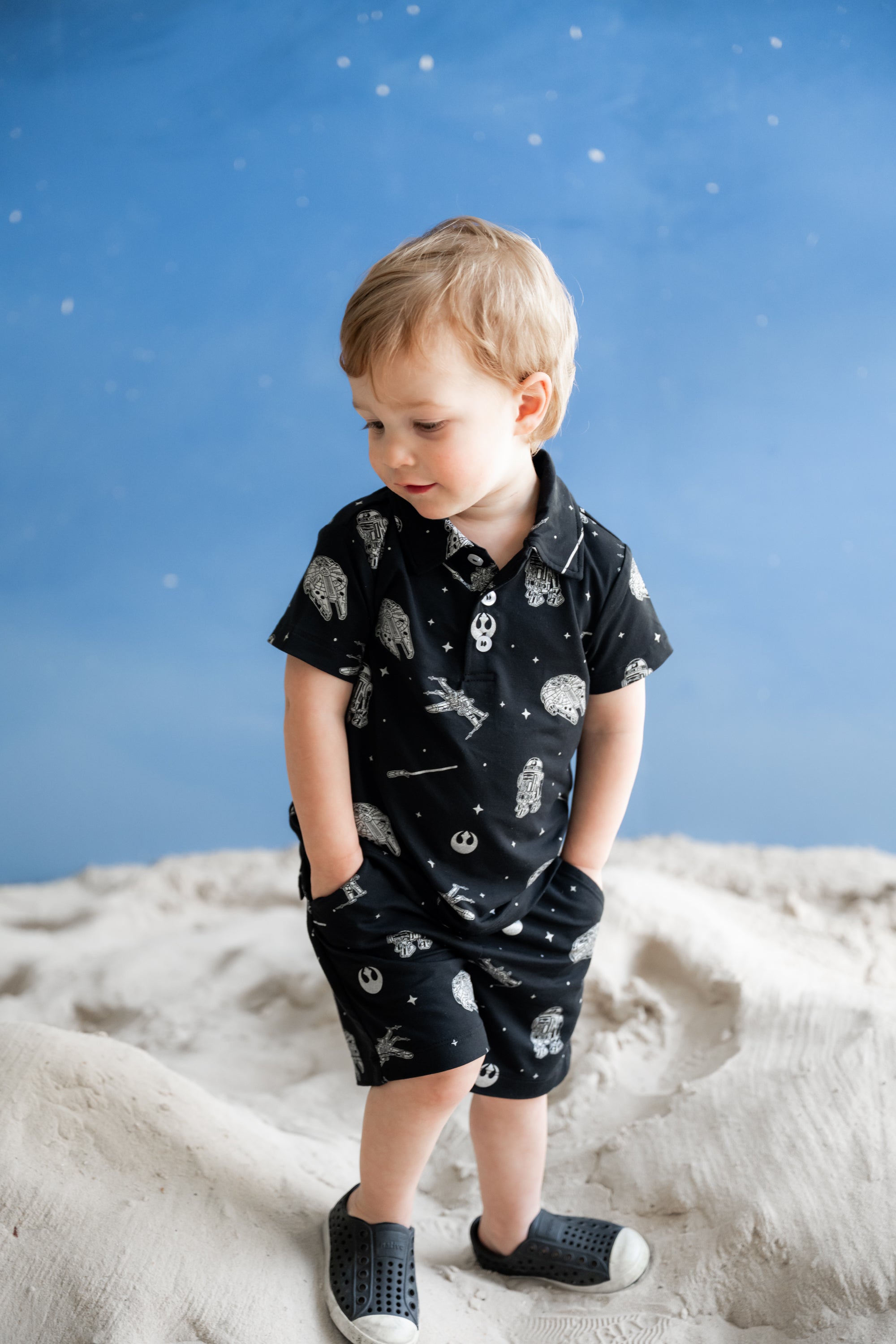 Young boy posing wearing hte Toddler Short Sleeve Polo in STAR WARS™ standing in sand simulating the moon