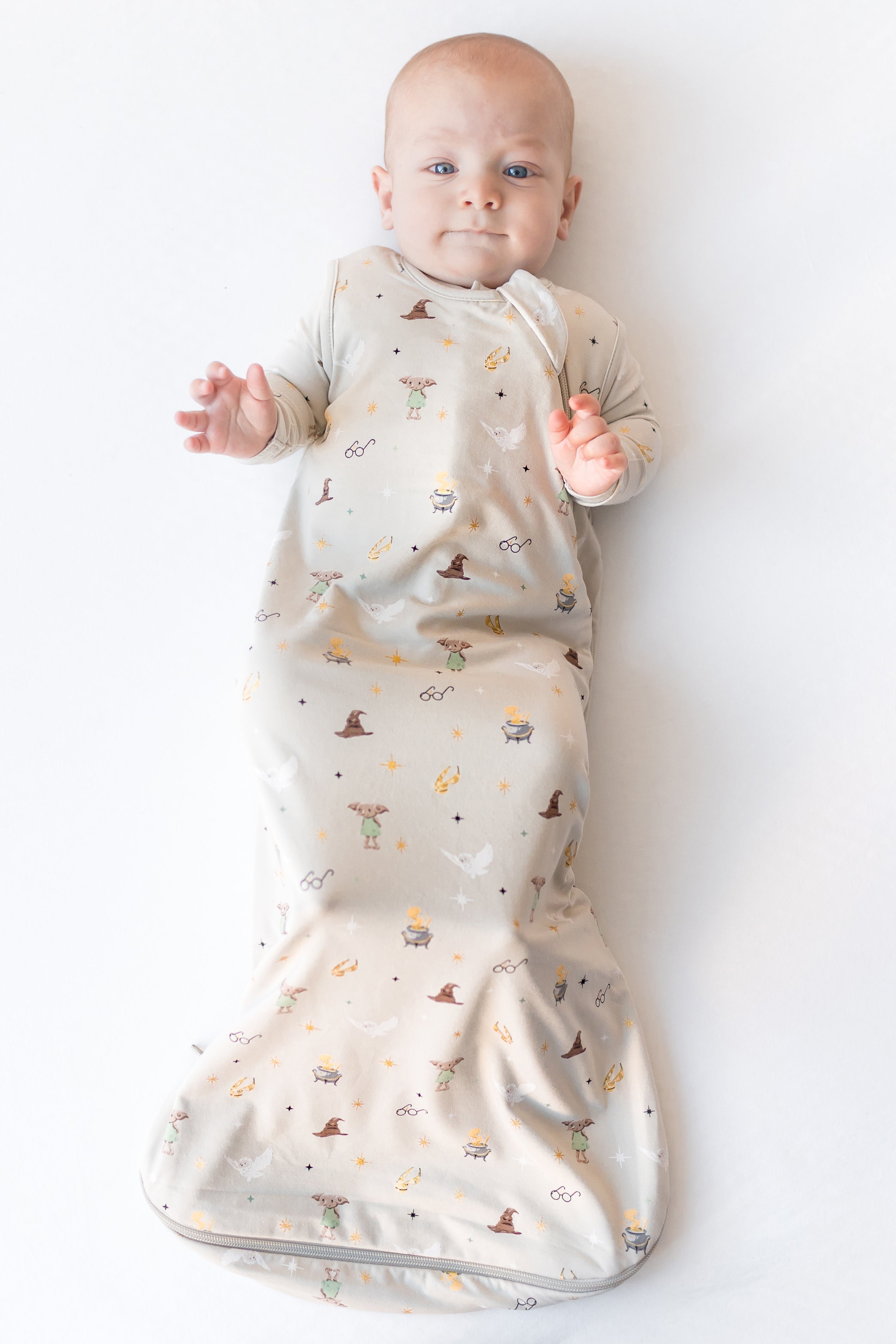 Baby in a cream sleep bag with Harry Potter prints on a white background.