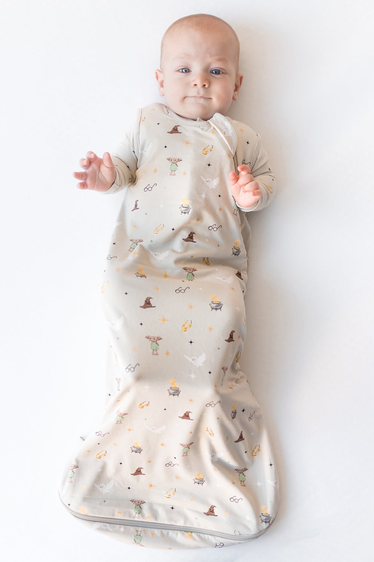 Baby in a cream sleep bag with Harry Potter prints on a white background.