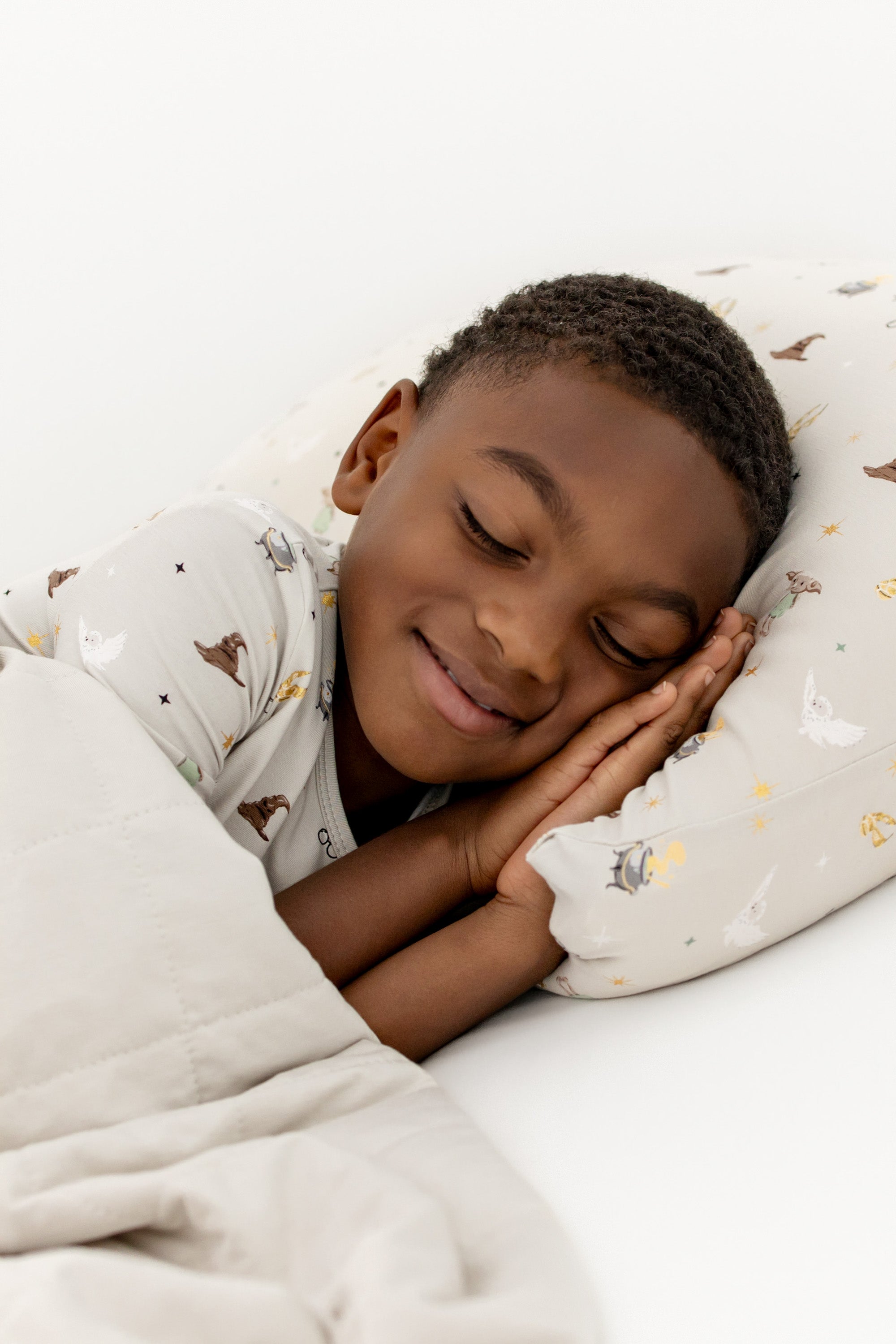 Child sleeping with a cream standard pillowcase with Harry Potter prints on a white sheet, under cream youth blanket.