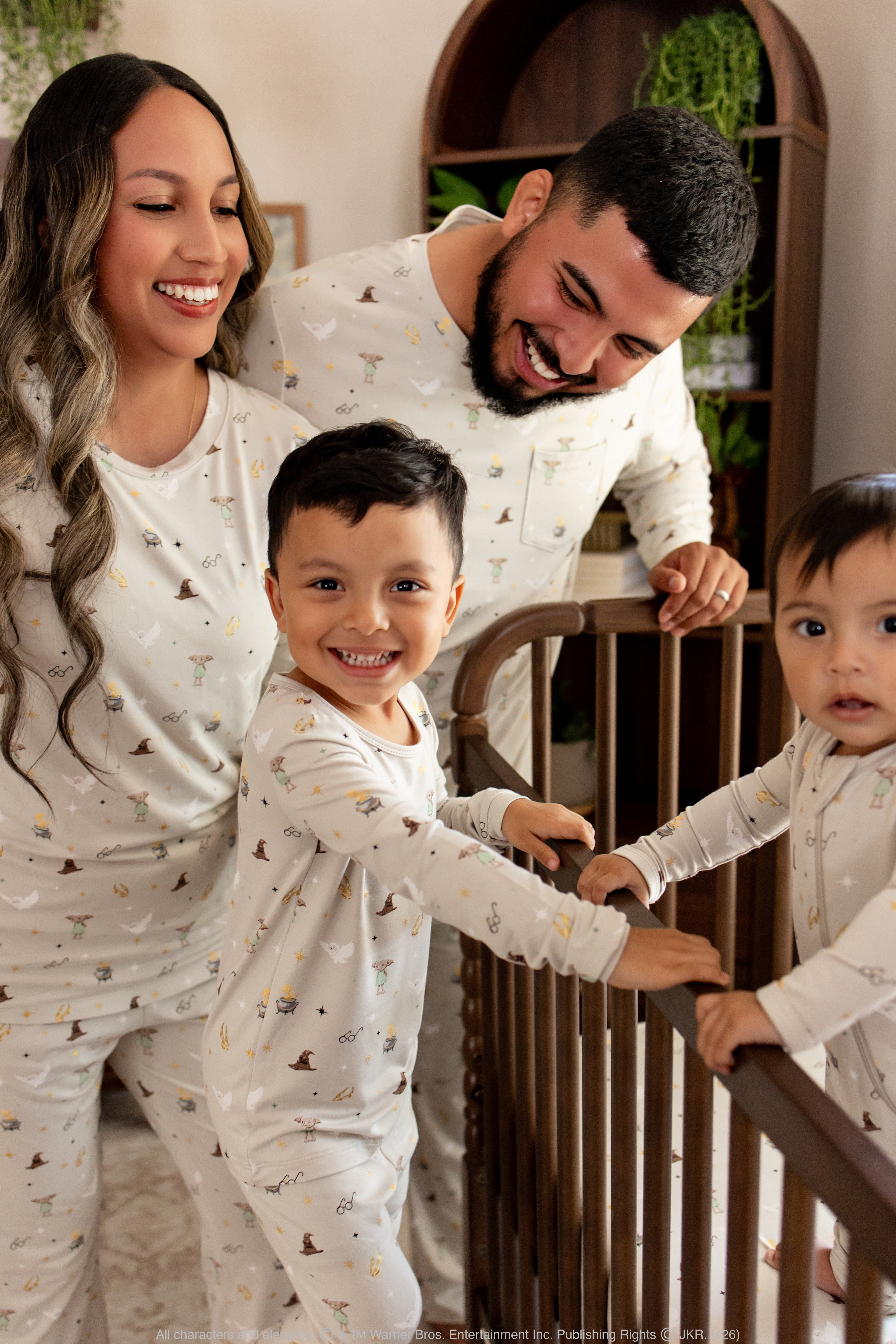 Family of 4 standing around a wooden crib wearing matching bamboo harry potter inspired pajamas 