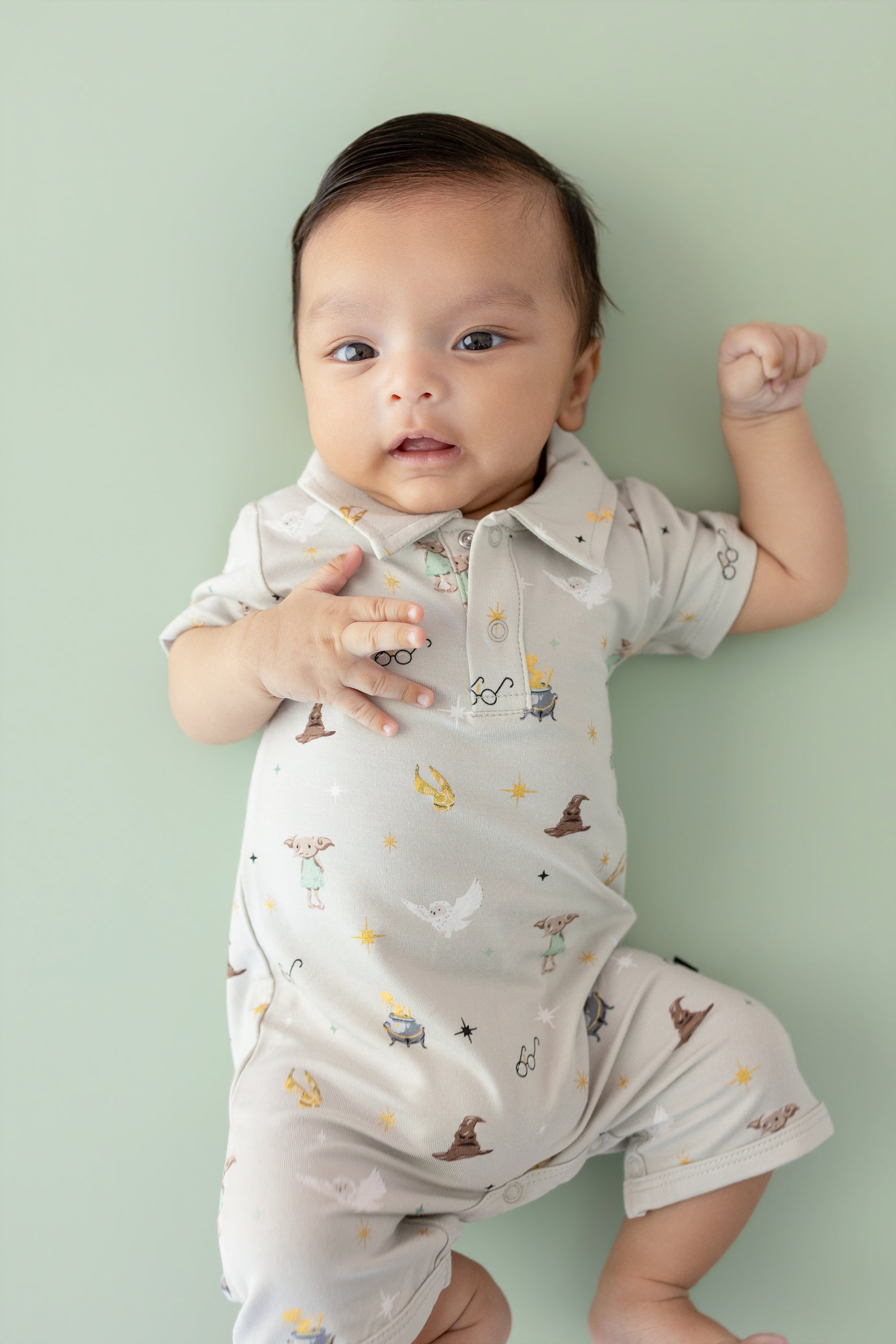 Baby wearing a cream polo shortall with Harry Potter prints on a green background