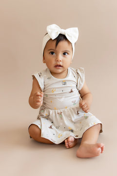 Child wearing a Harry Potter patterned twirl bodysuit dress with a white bow headband on a beige background