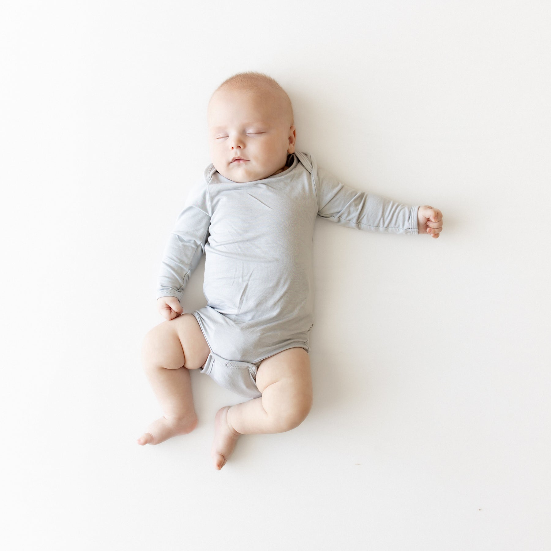 Baby in a gray onesie lying on a white surface