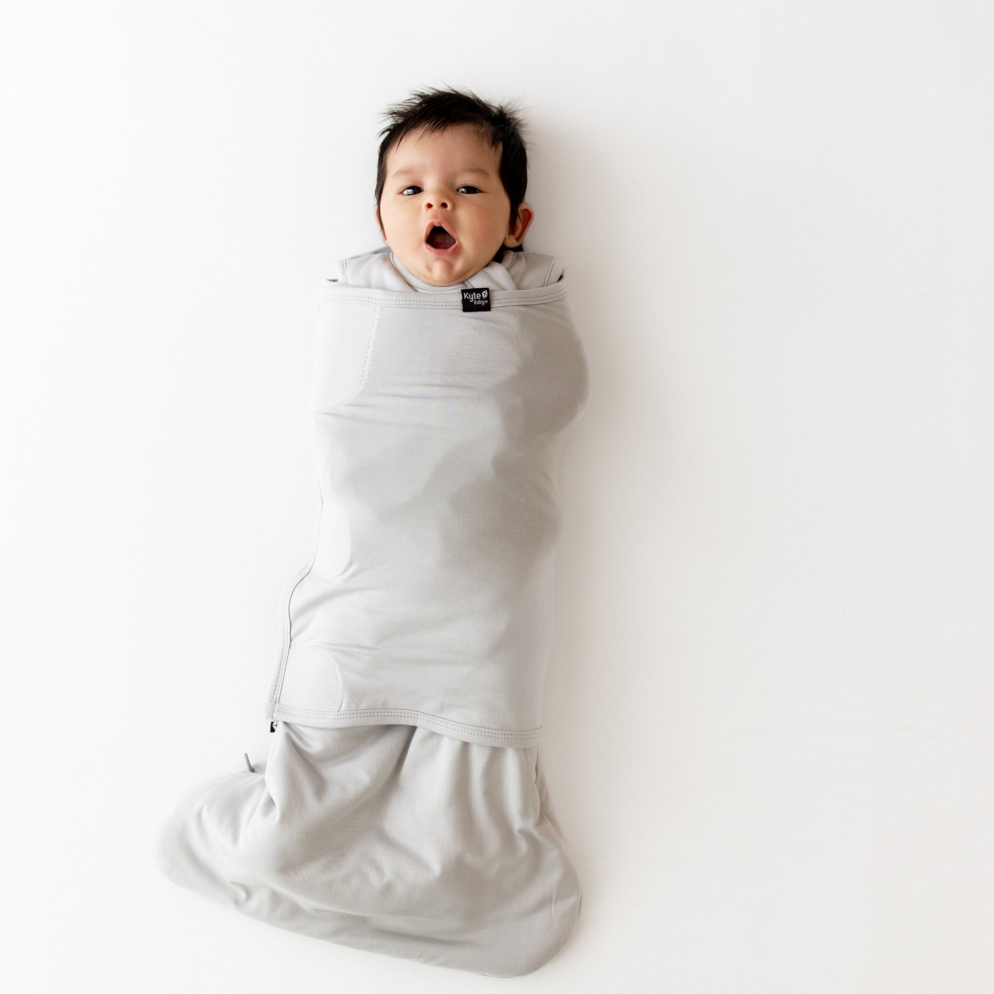 Baby yawning and wrapped in a gray swaddler on a white background