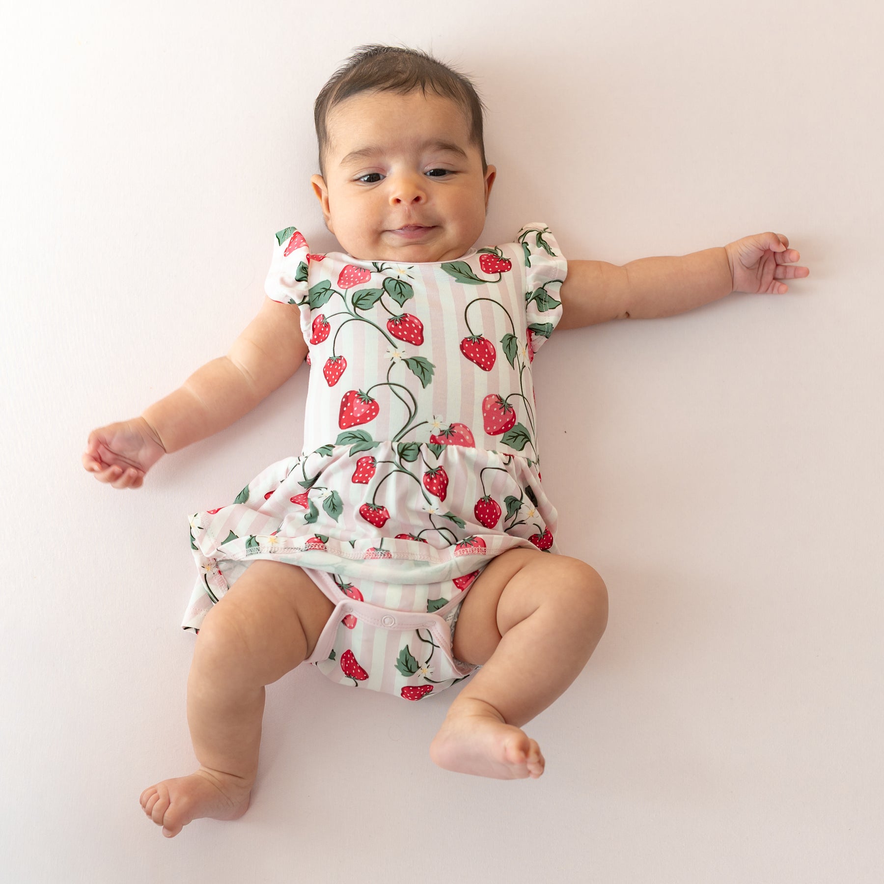 Young infant wearing the soft and breathable Twirl Bodysuit Dress in Strawberry Fields on a light pink surface