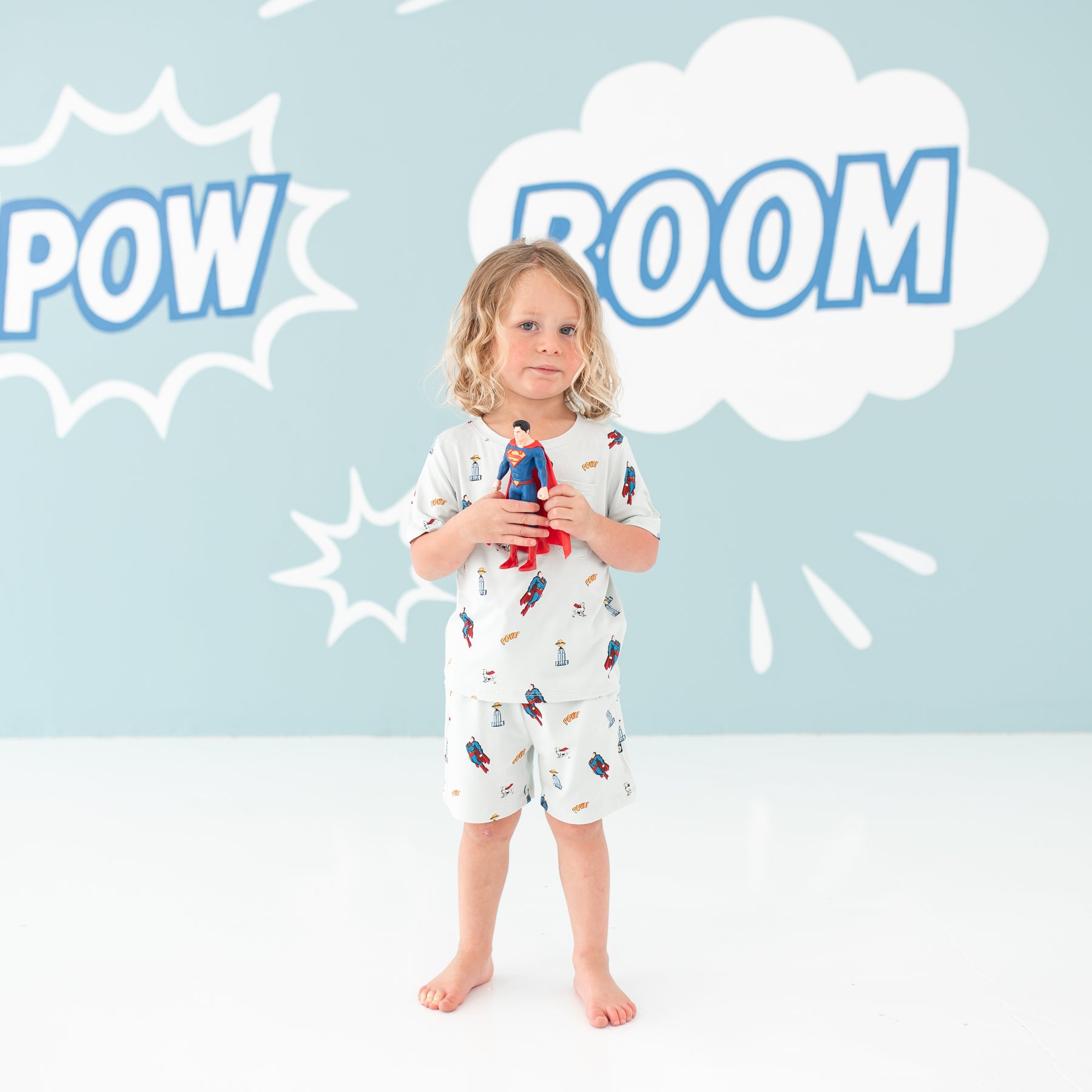 Child model holding a Superman action figure wearing the Drawstring Short in Superman™ and matching Crew Neck Tee