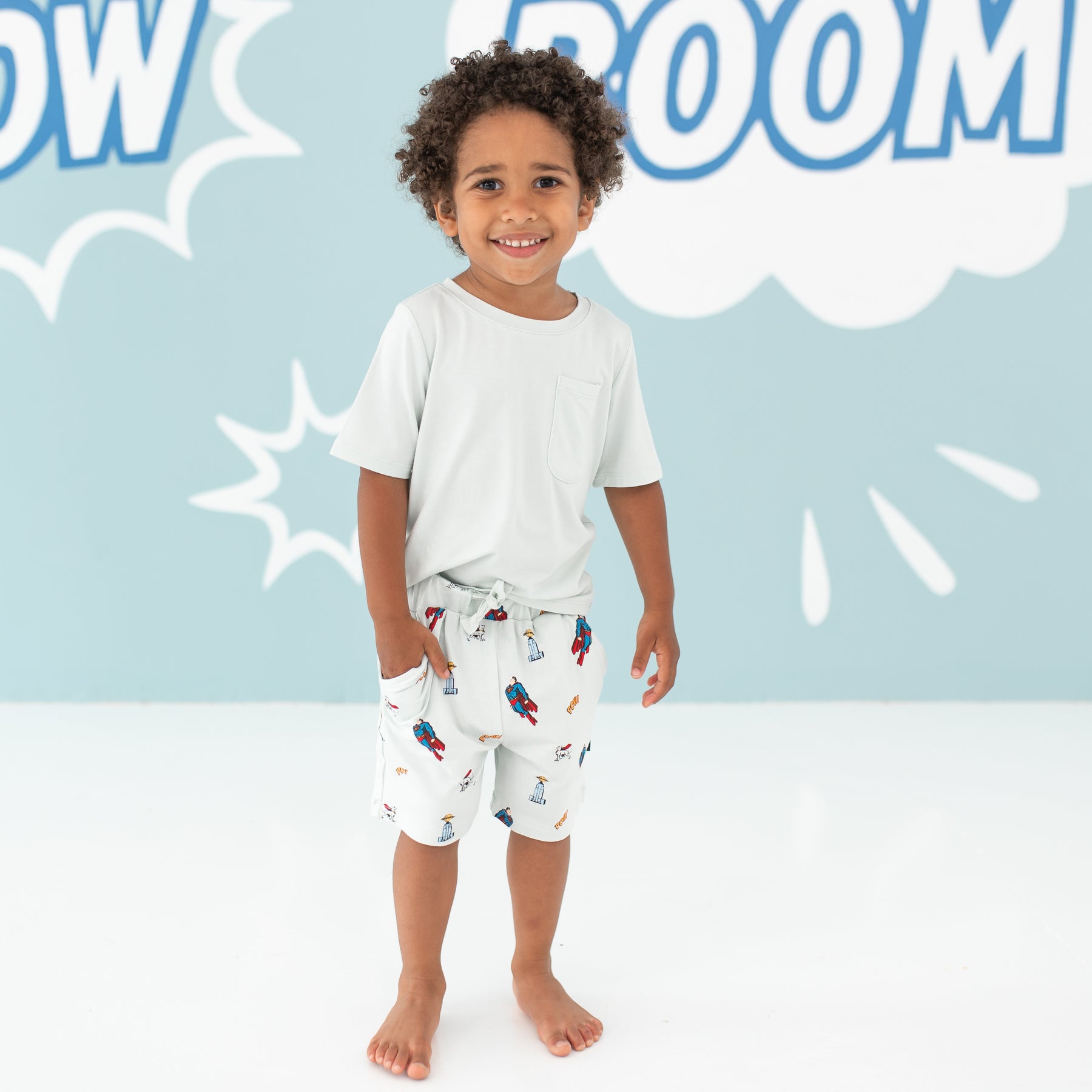 Child model standing with his hand in his Drawstring Short in Superman™ pocket paired with a Toddler Crew Neck Tee in Dew
