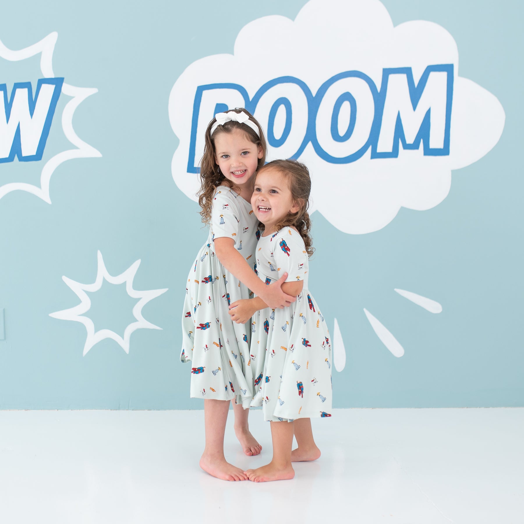 Two girl models hugging one another wearing the Twirl Dress in Superman™