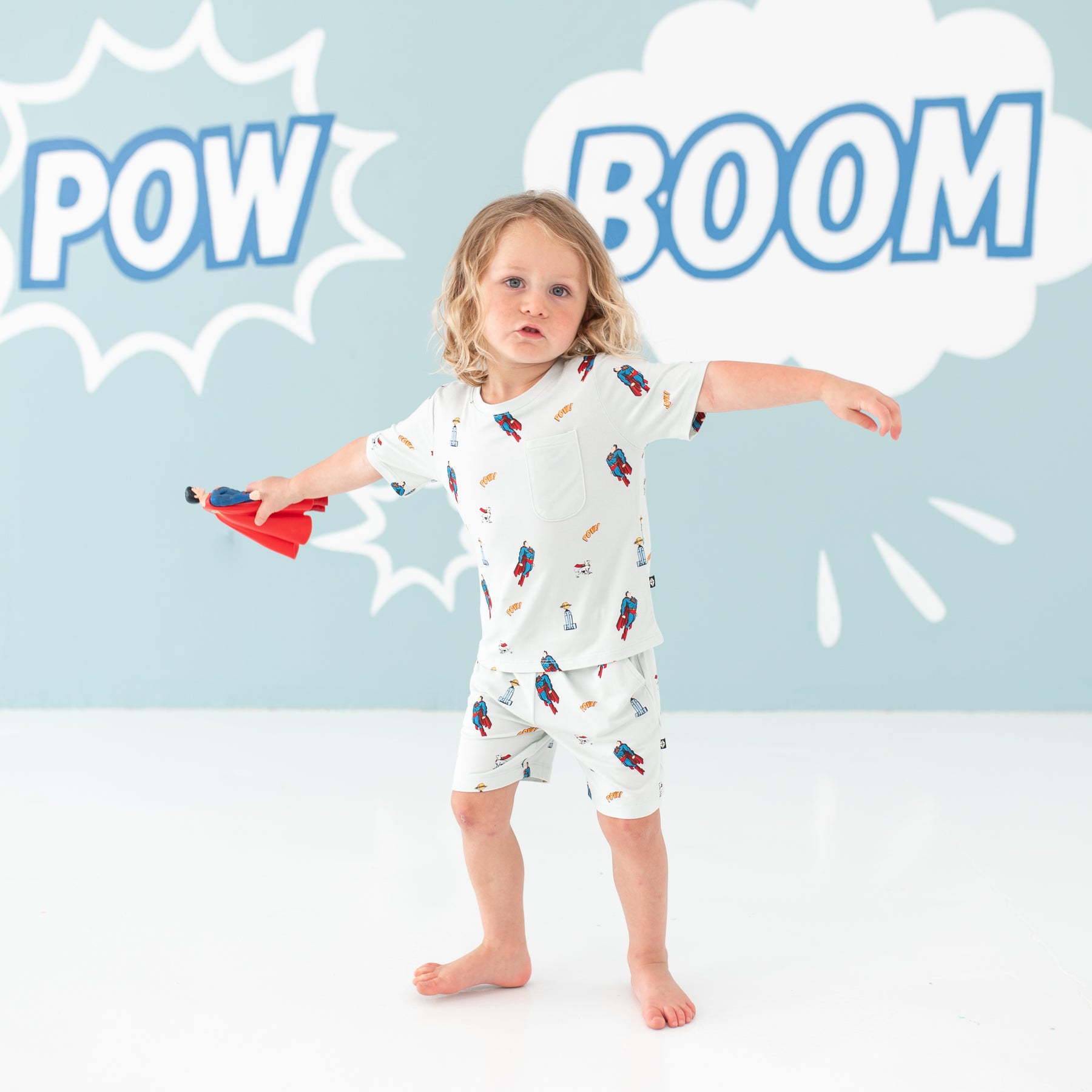 Toddler spinning holding a Superman action figure wearing the Toddler Crew Neck Tee in Superman™ and matching drawstring shorts