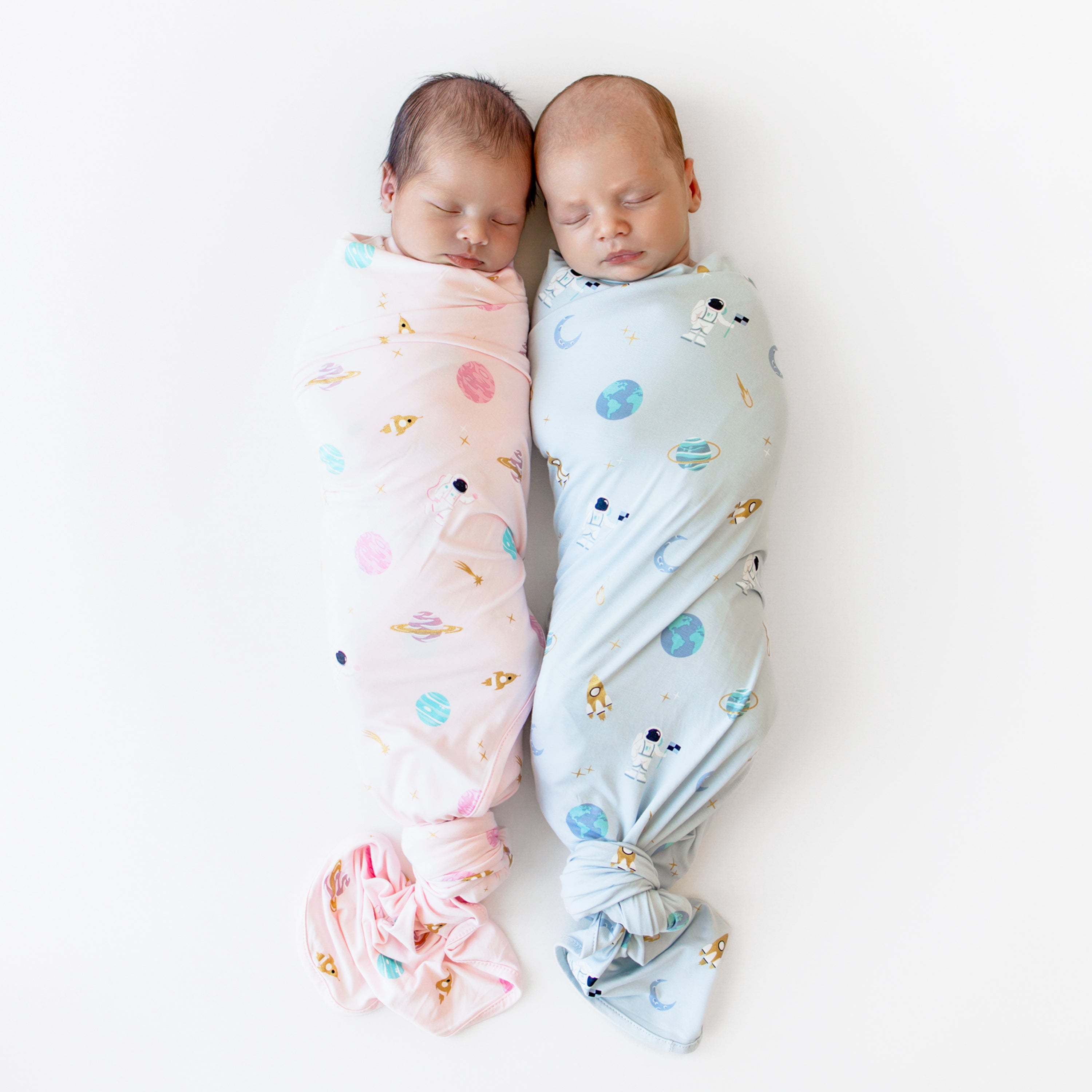 two babies laying swaddled in ice and sakura space swaddle blankets