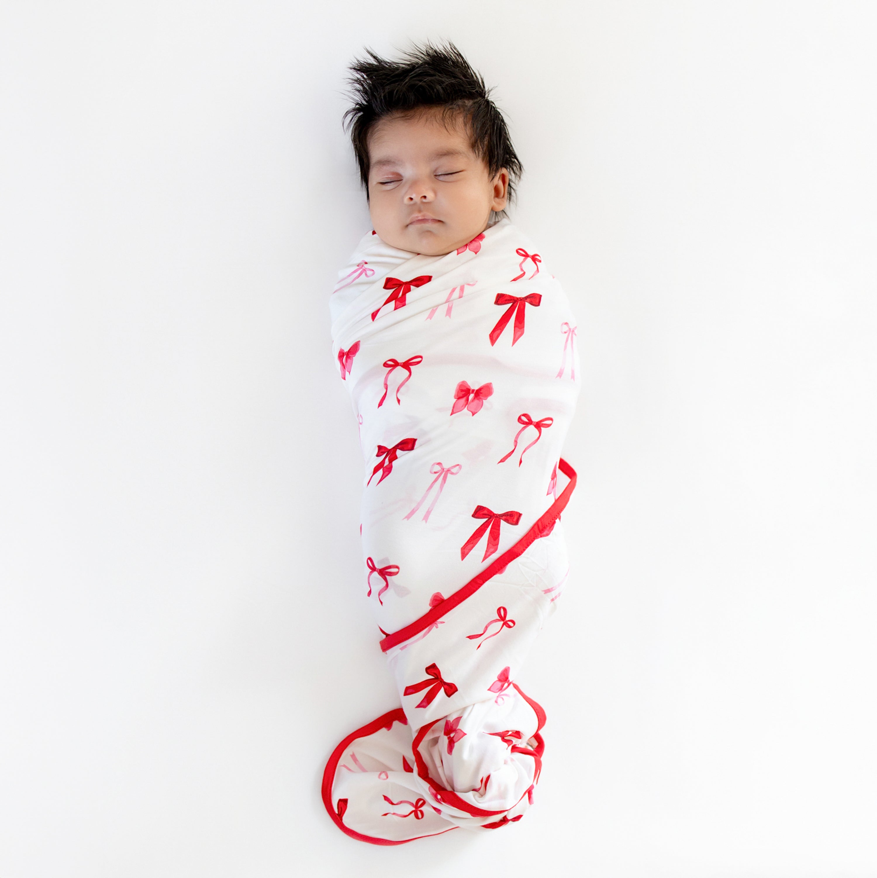 Newborn sleeping swaddled in the soft and stretchy Swaddle Blanket in Small Love Bow