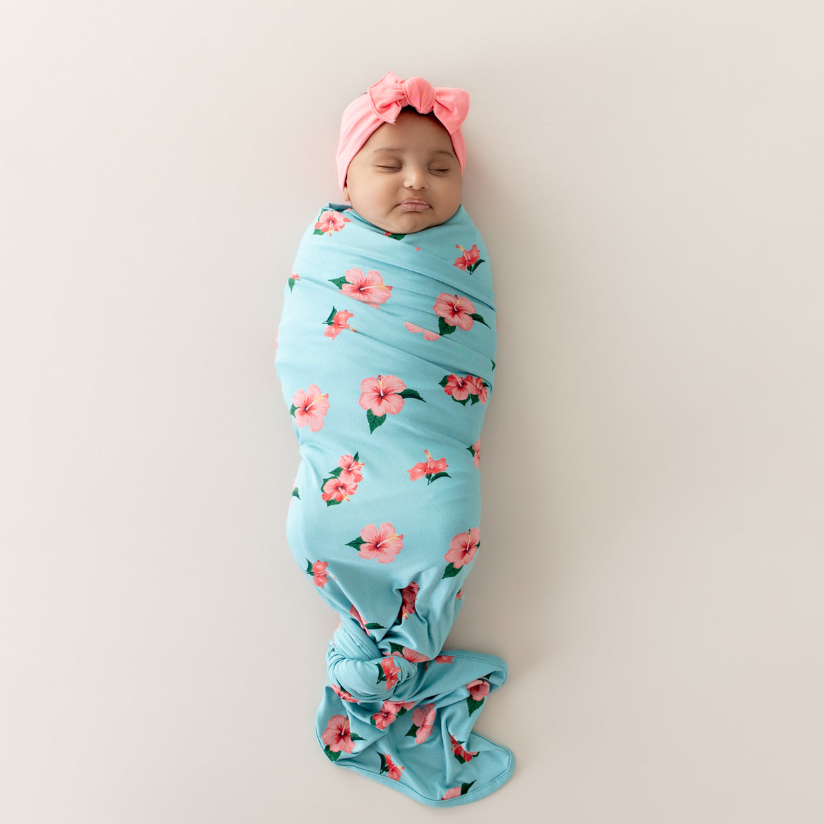 Baby swaddled in Kyte Swaddle Blanket in Hibiscus wearing Guava bow