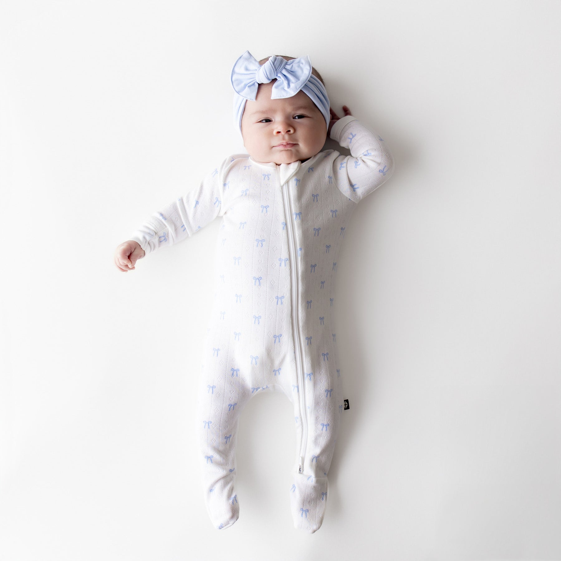 baby in a white pointelle footie with blue bow pattern on a white background