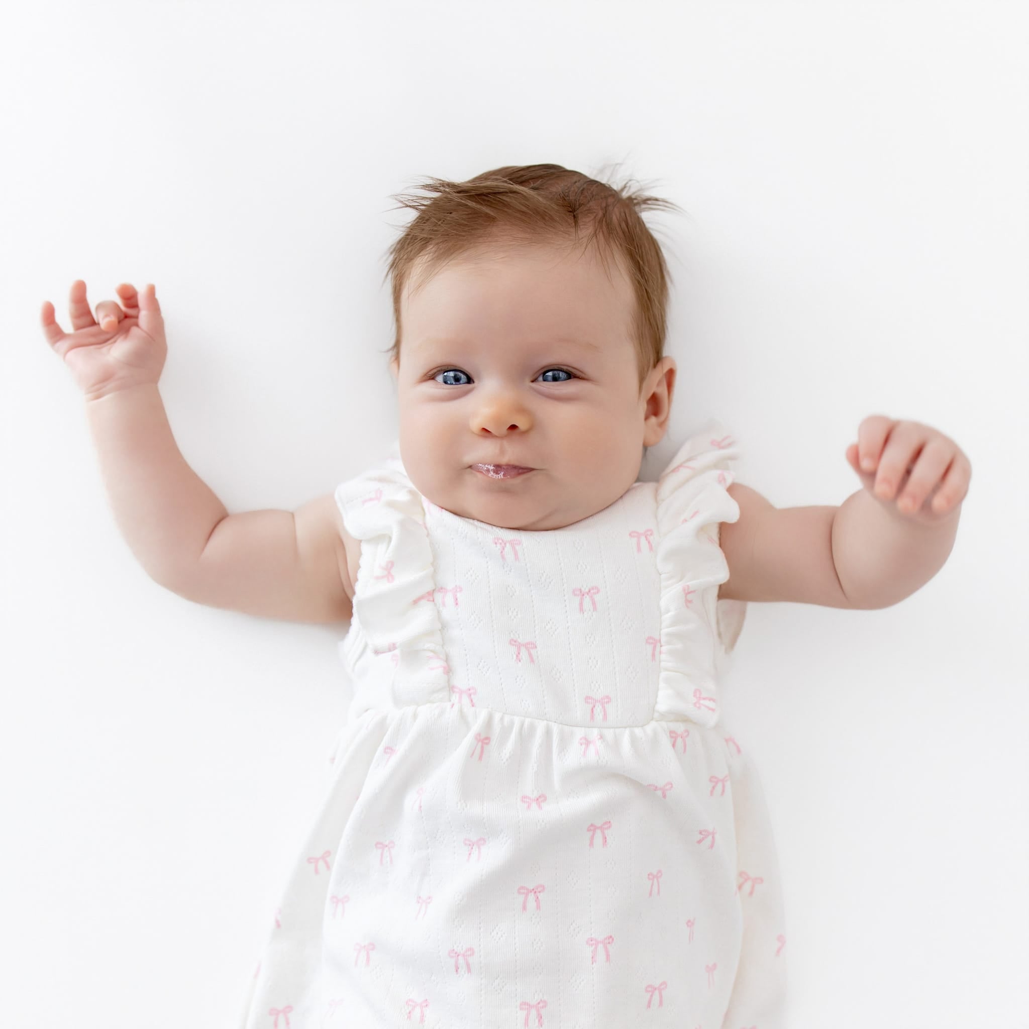 Baby in a white dress with ruffles and subtle pink bow pattern