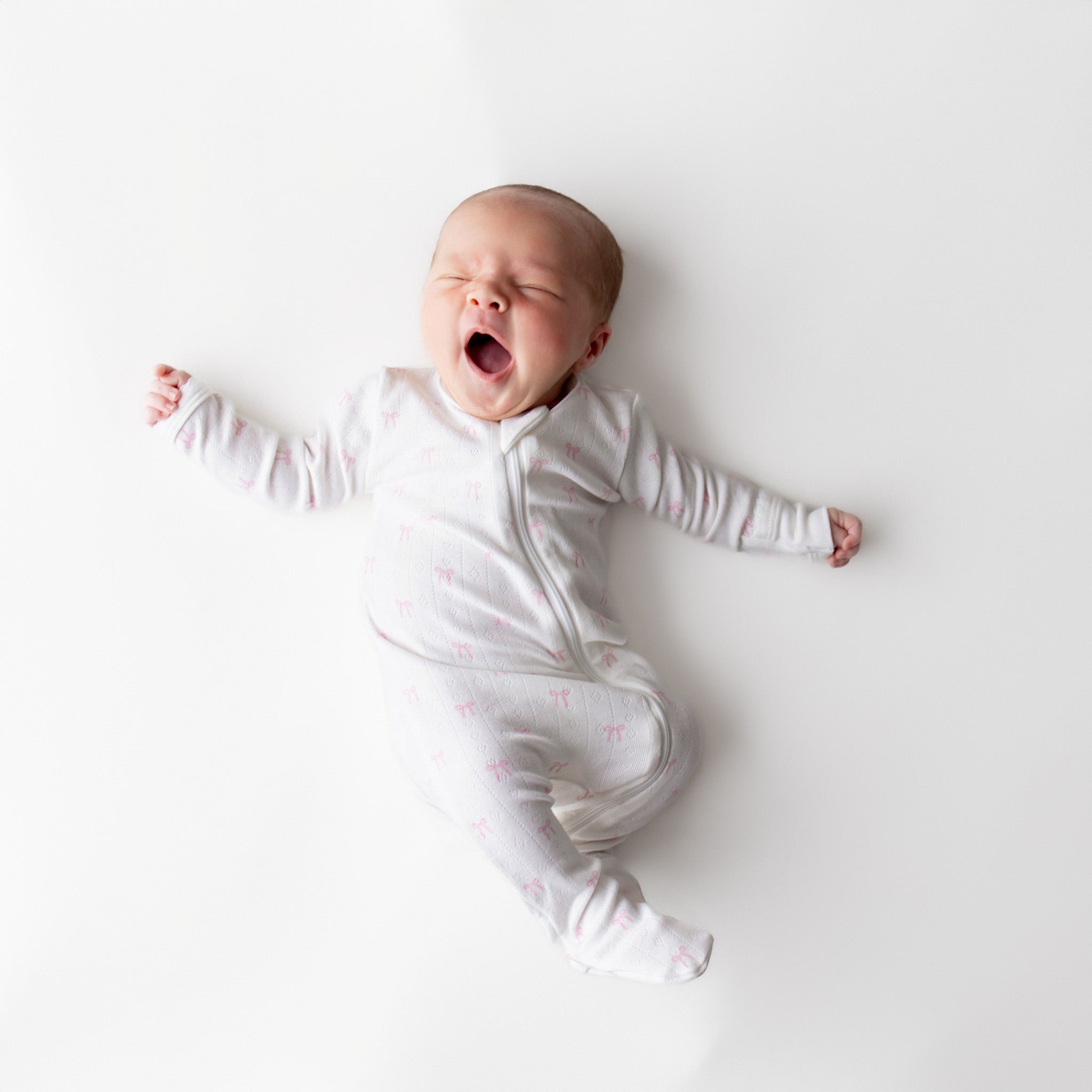 Baby in a white onesie with pink bows on a white background
