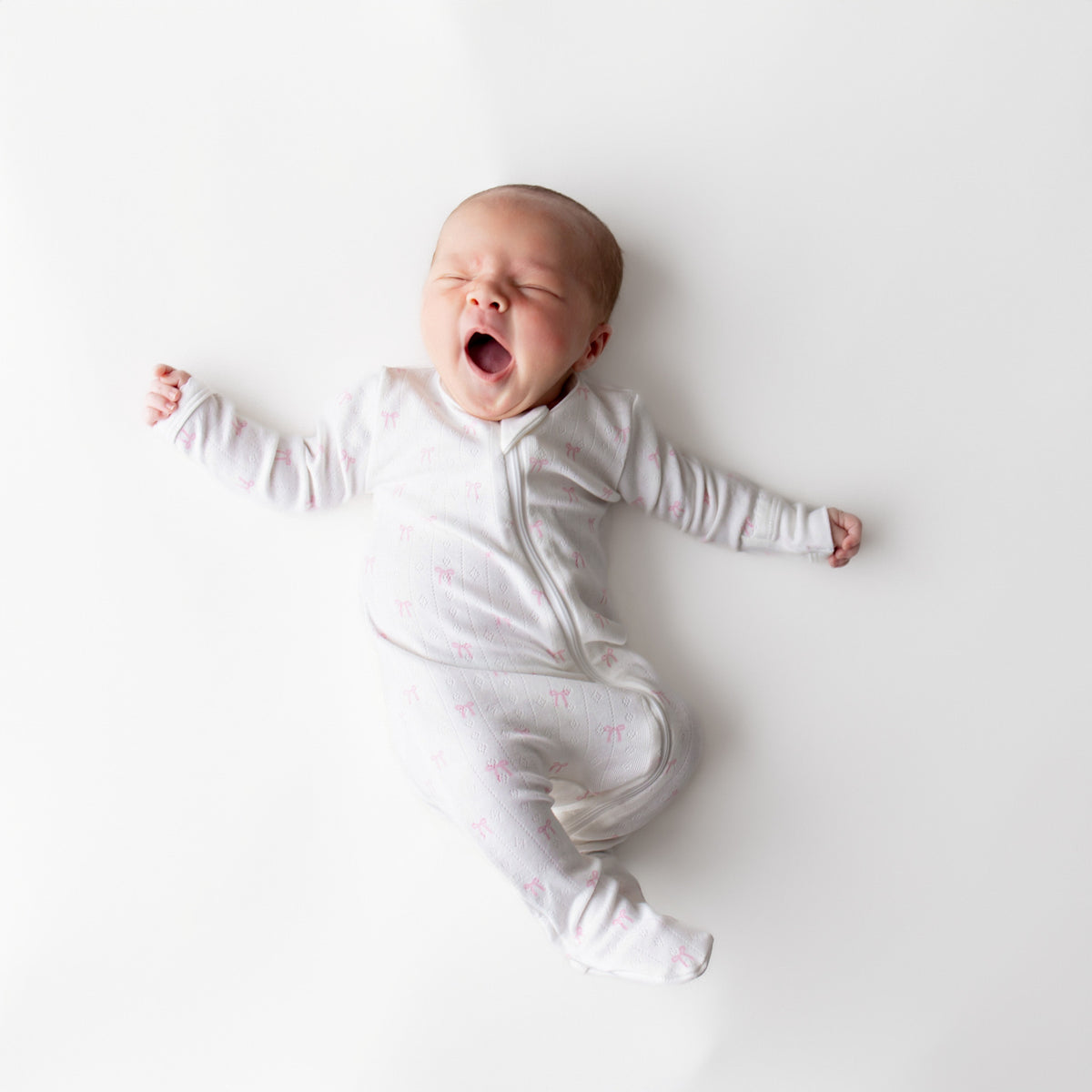 Baby in a white onesie with pink bows on a white background
