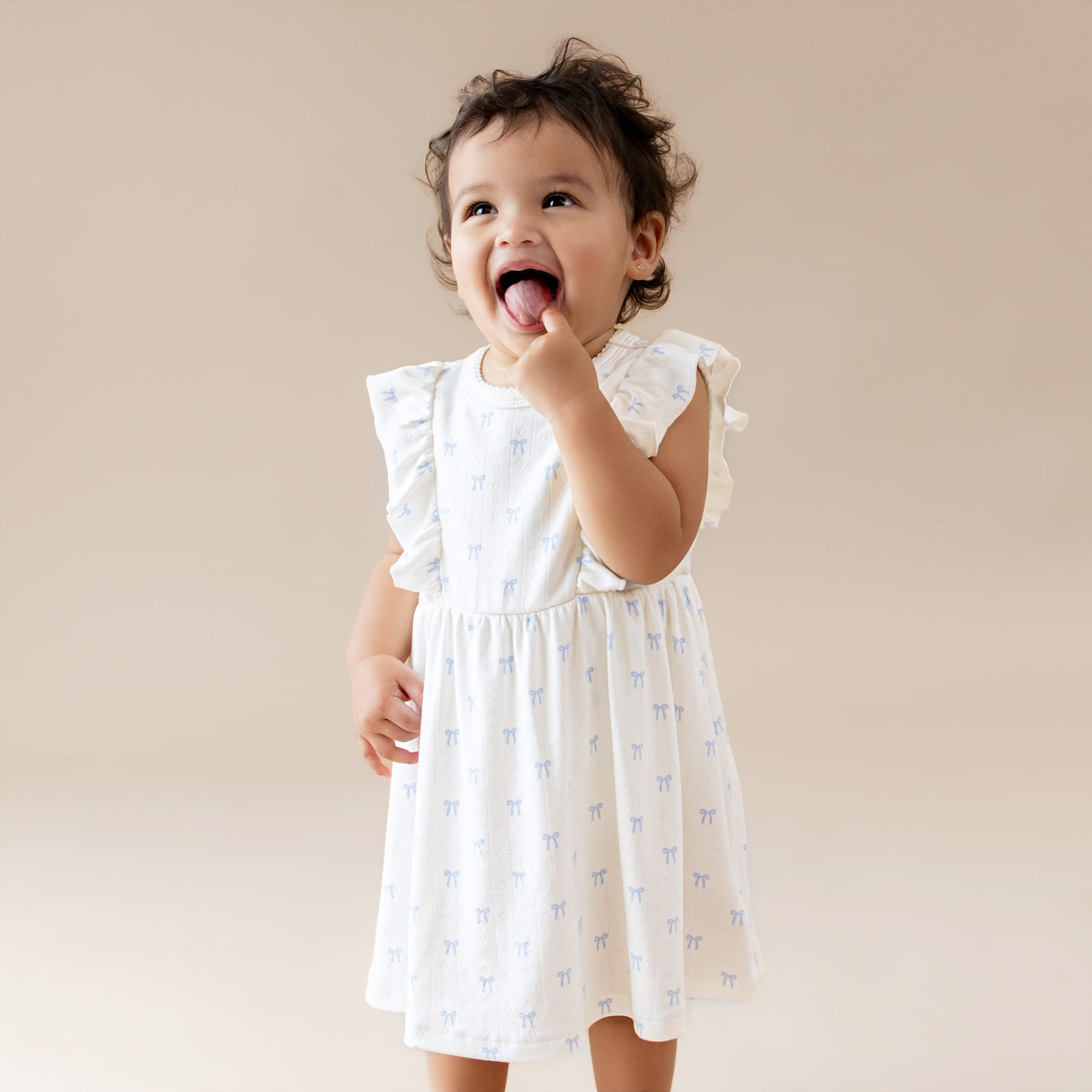 Child wearing a white dress with ruffled sleeves and blue bow pattern on a beige background