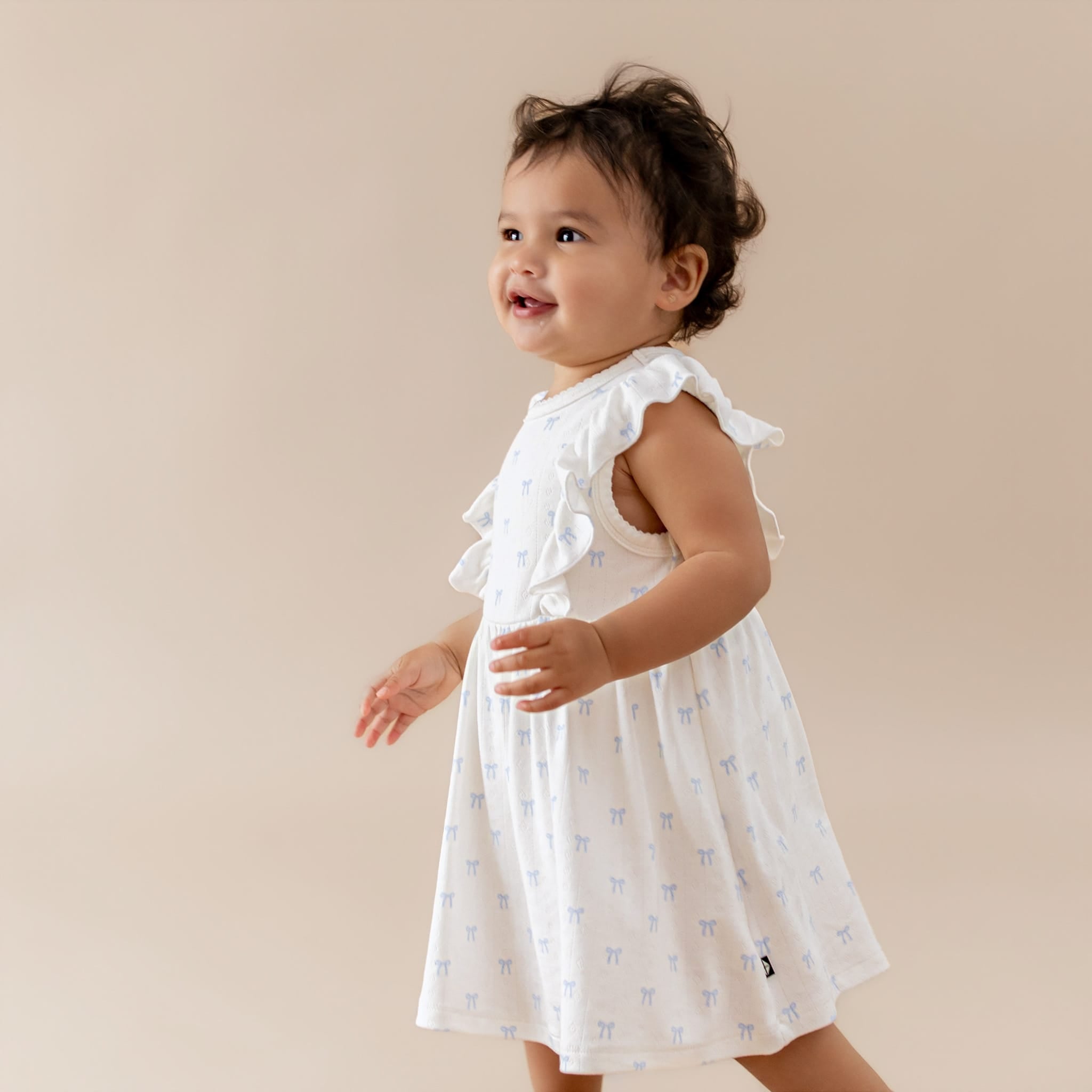 Baby girl in a white dress with ruffles and blue bow pattern on a beige background