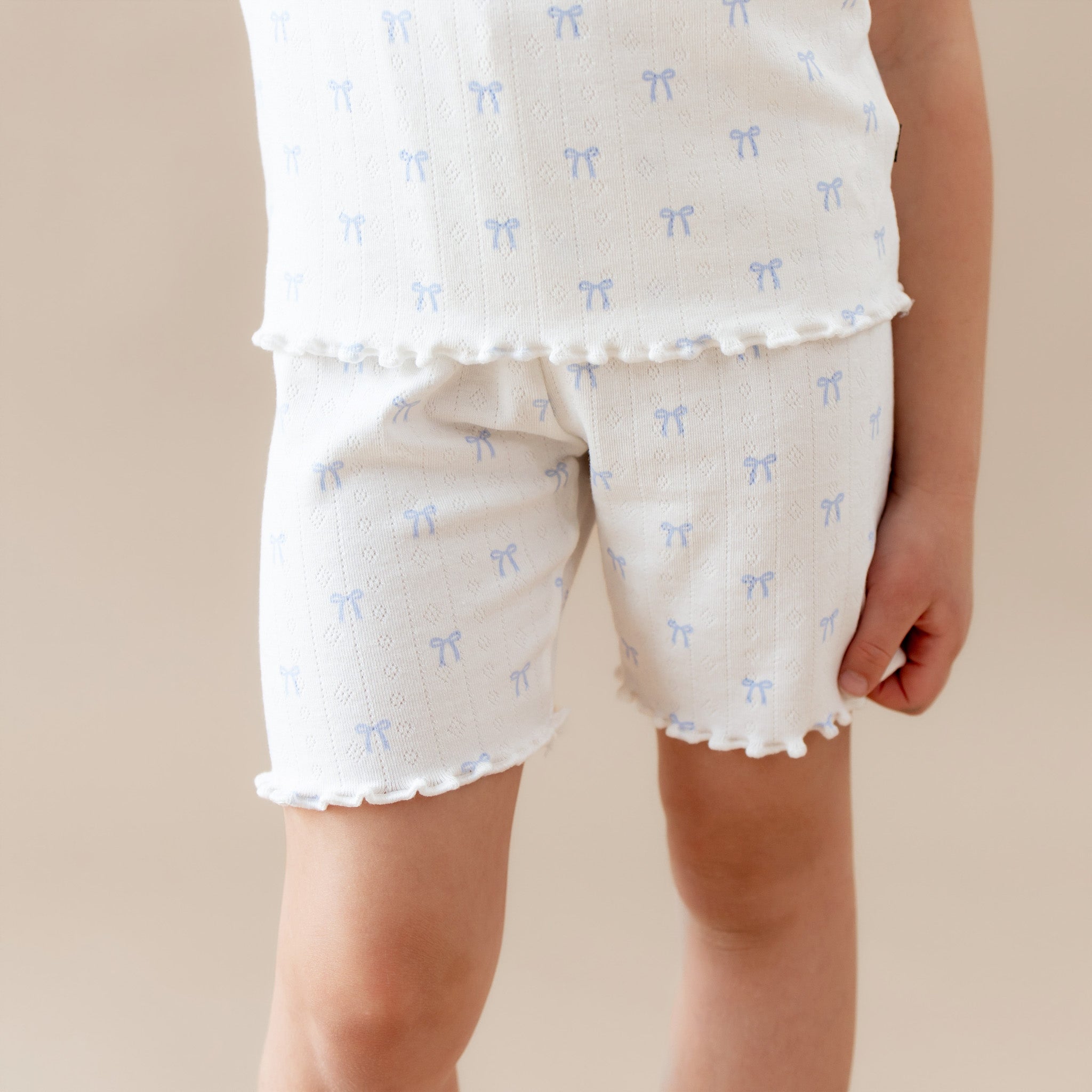 Children's lounge set with white top and shorts featuring blue bow patterns on a beige background.