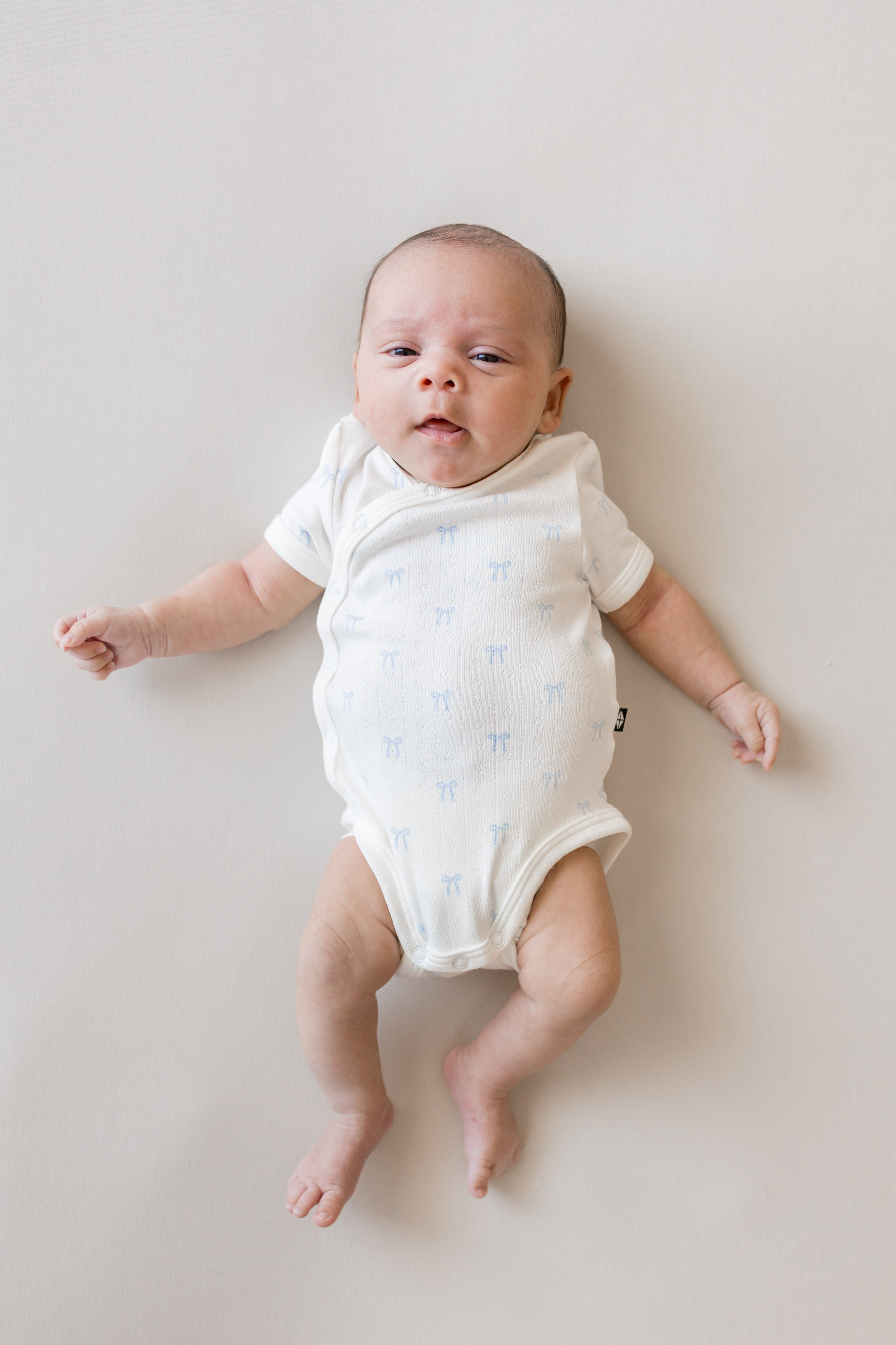 Baby wearing Pointelle Kimono Bodysuit in Sweet Blue Bow print on a beige background