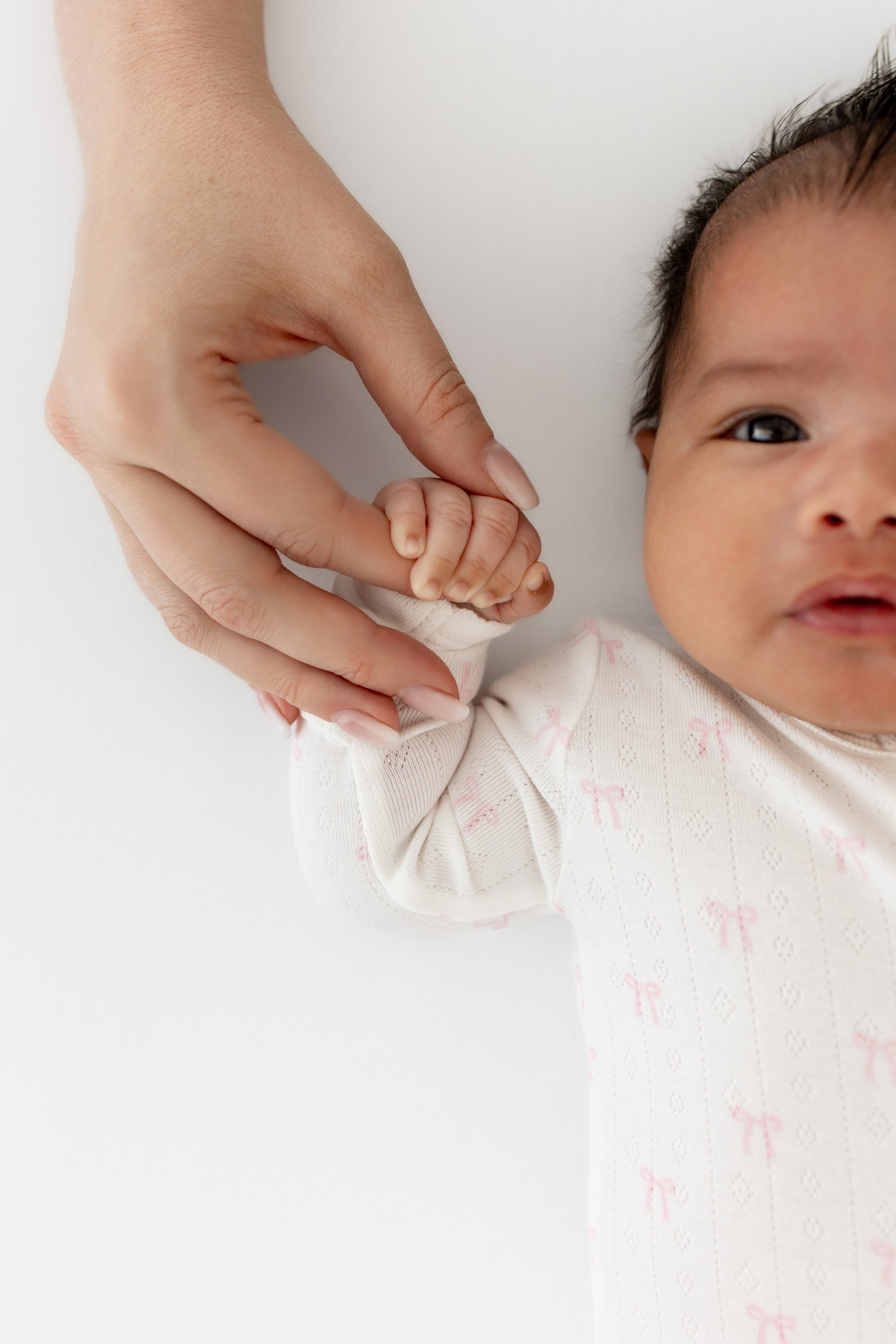 Close up of the arm on the Pointelle Zippered Footie in Sweet Pink Bow shown on an infant holding her mothers hand