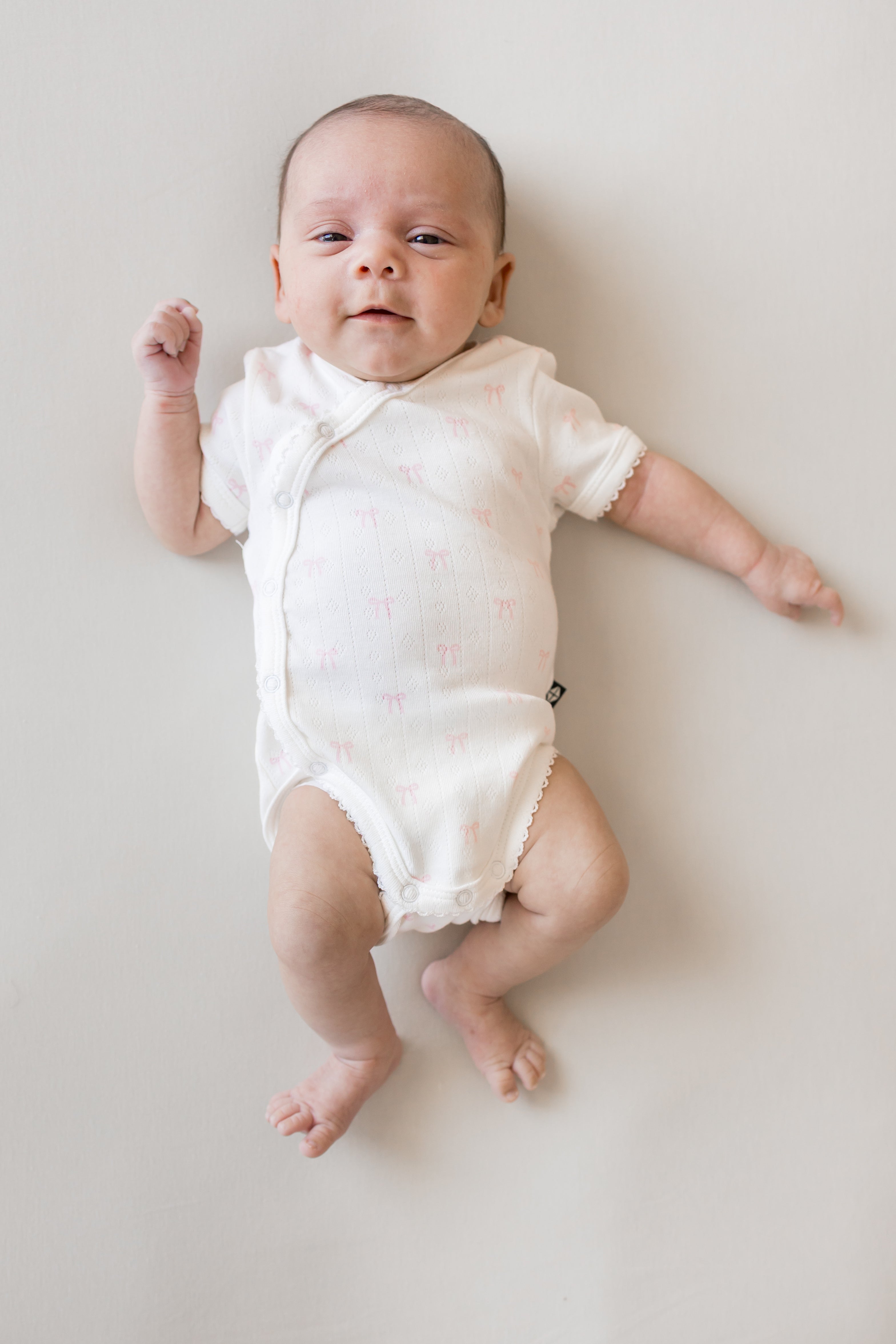Baby wearing Pointelle Kimono Bodysuit in Sweet Pink Bow print on a beige background