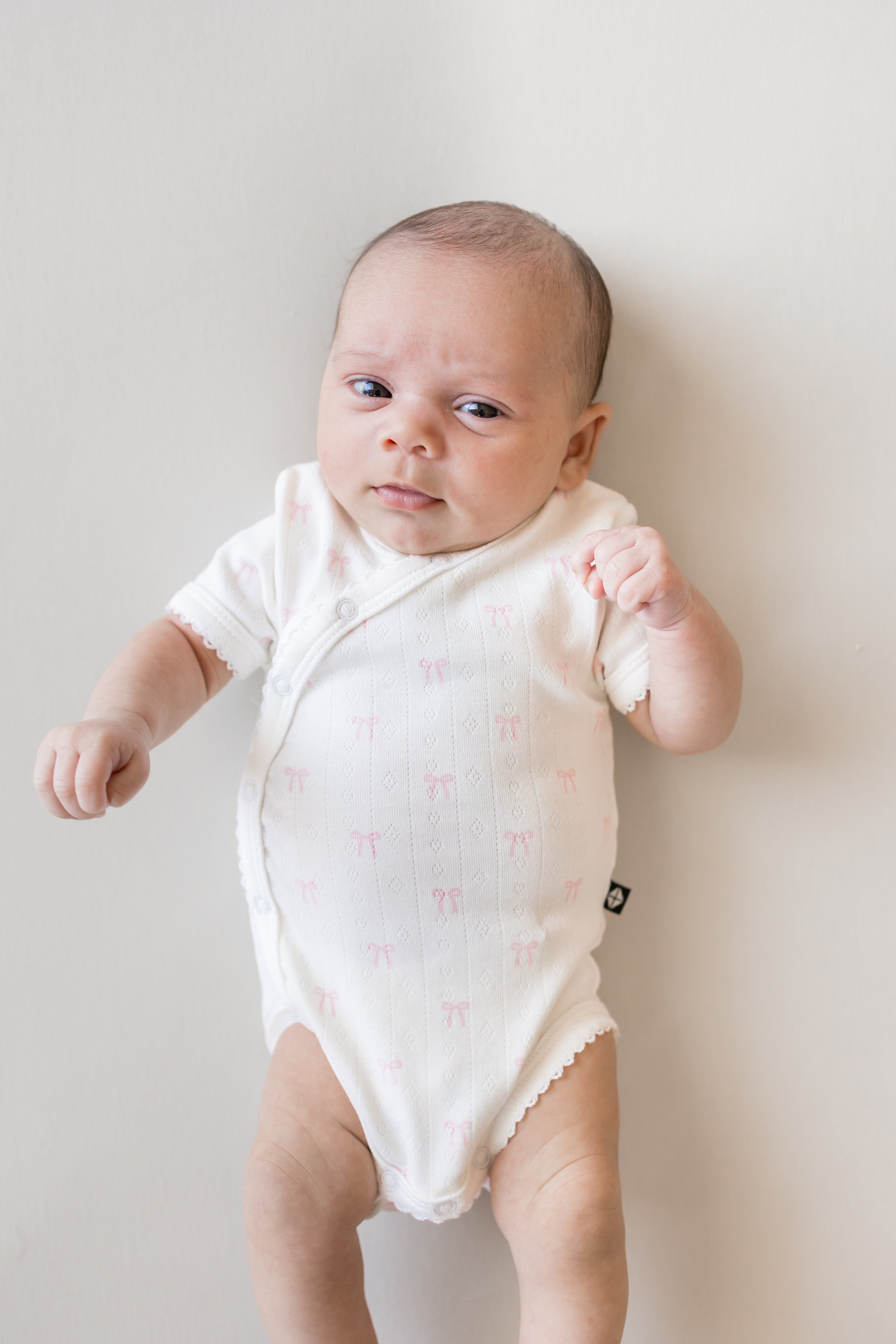 close up of Baby wearing Pointelle Kimono Bodysuit in Sweet Pink Bow print on a beige background