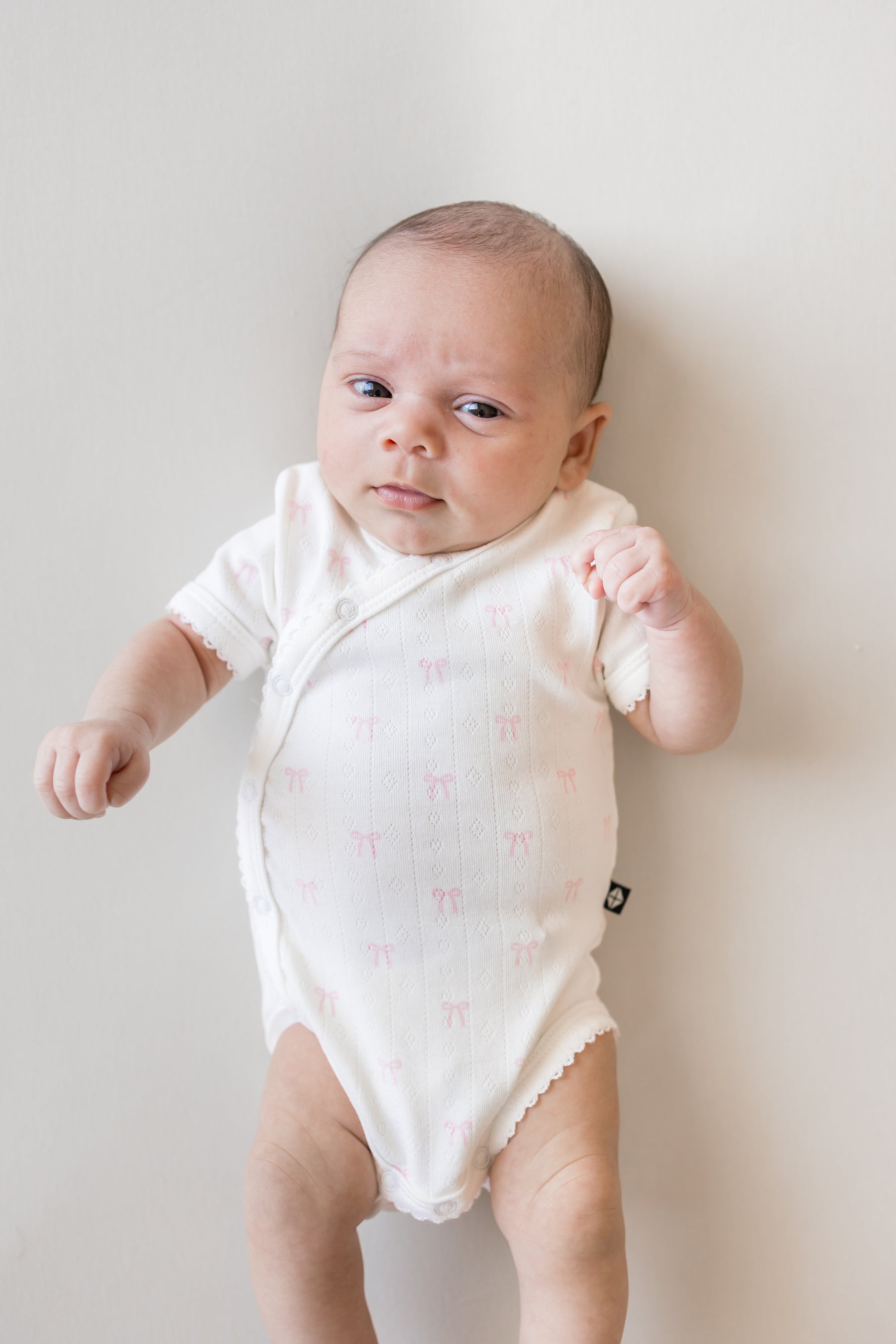 close up of Baby wearing Pointelle Kimono Bodysuit in Sweet Pink Bow print on a beige background