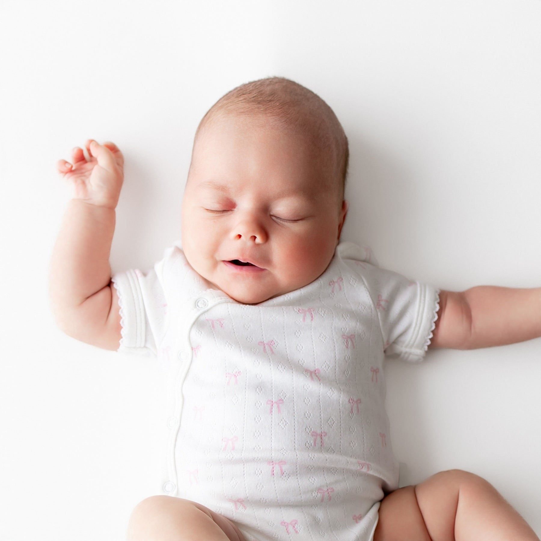 Baby wearing a white onesie with pink patterns on a white background