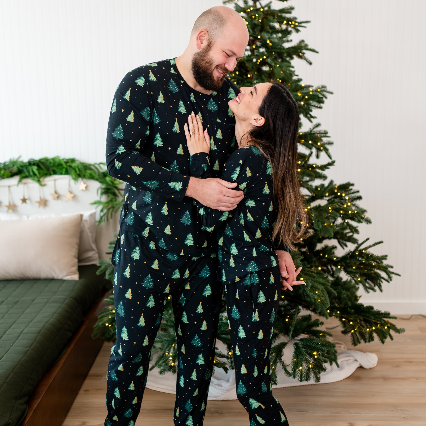 Wife standing with her husband with her hand on his chest both looking at one another matching in the Women's and Men's Jogger Pajama Set in Twinkle Tree