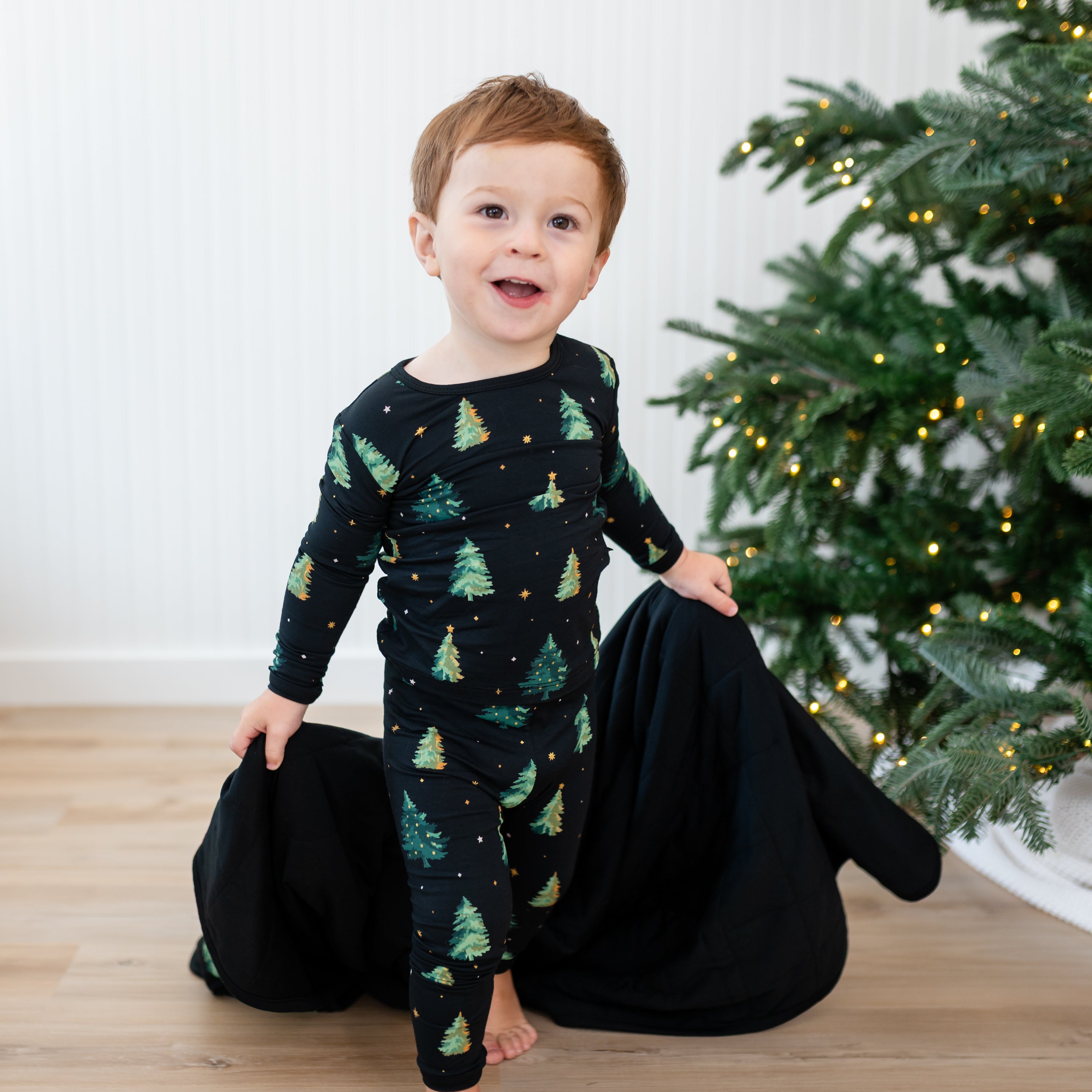 Young toddler walking wearing the Long Sleeve Pajamas in Twinkle Tree holding a Twinkle Tree blanket
