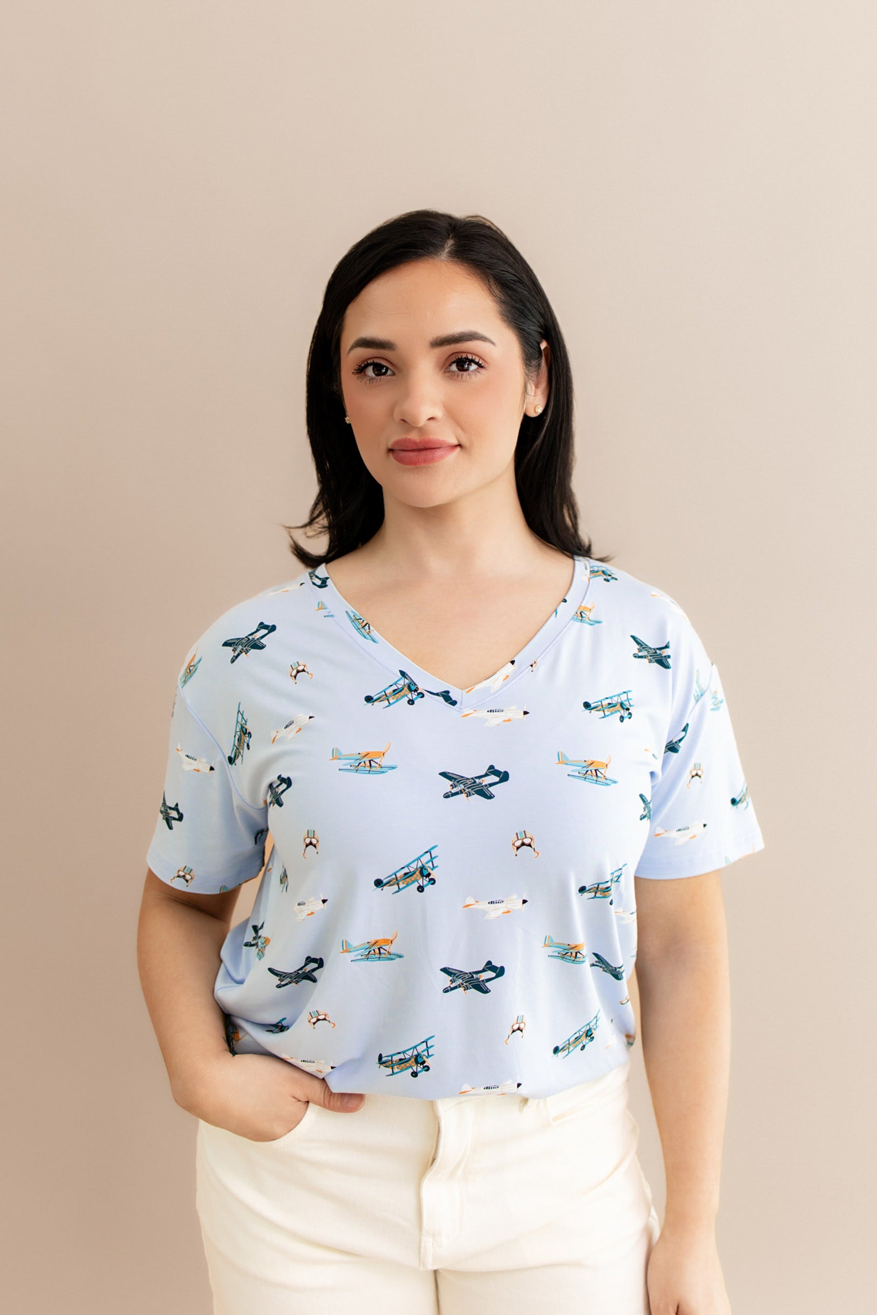 Smiling female wearing the Women's Relaxed Fit V-Neck in Take Off paired with cream pants