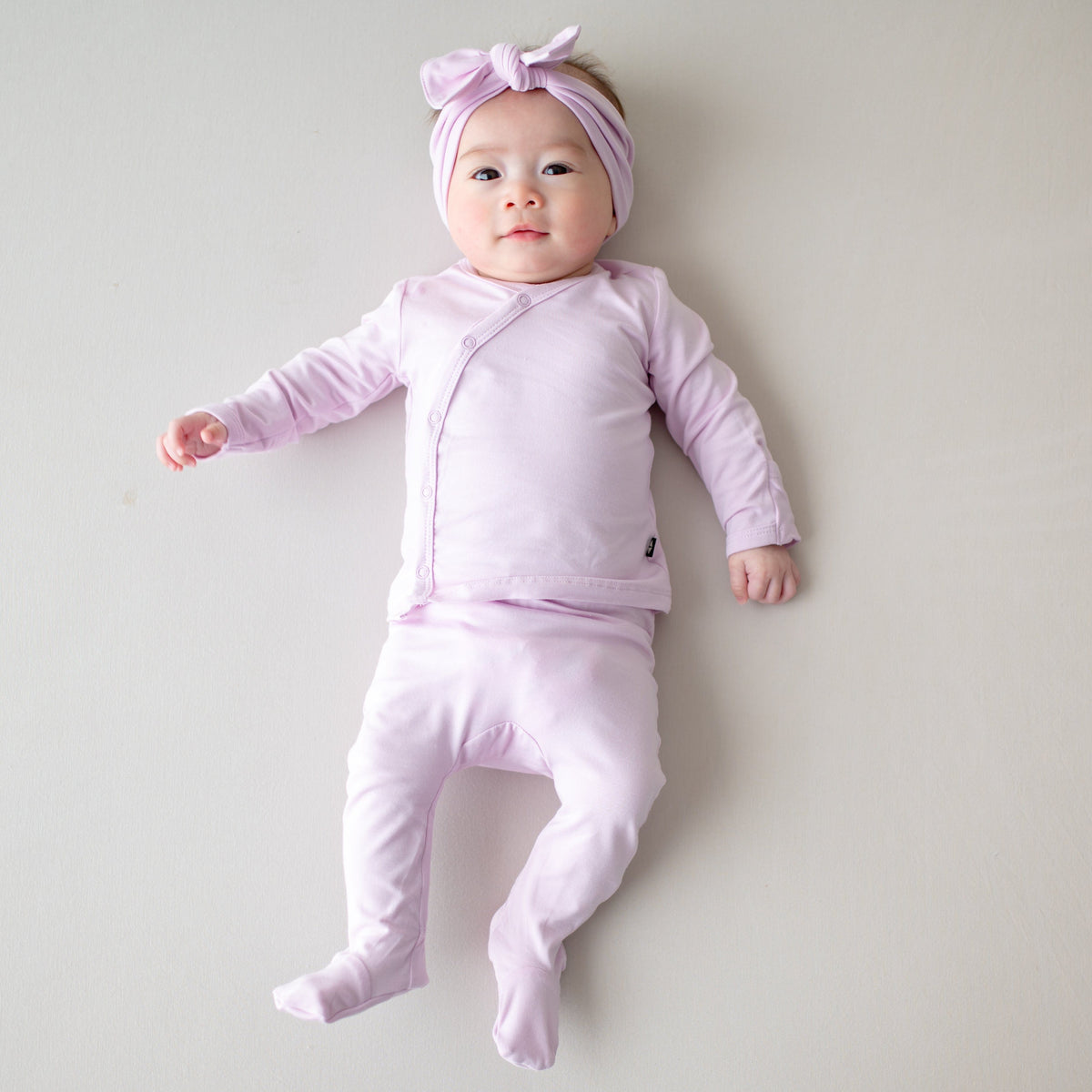 Newborn laying on a light neutral surface wearing the Take Me Home Set with Bow in Thistle