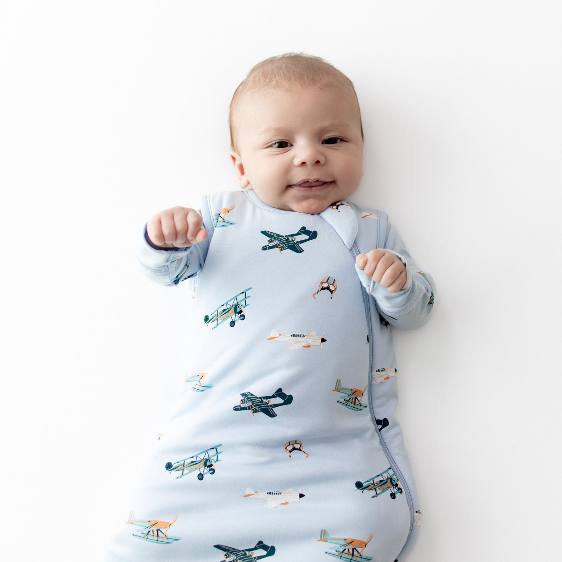 Close up of an infant wearing the Sleep Bag in Take Off 1.0 with a matching long sleeve romper on underneath