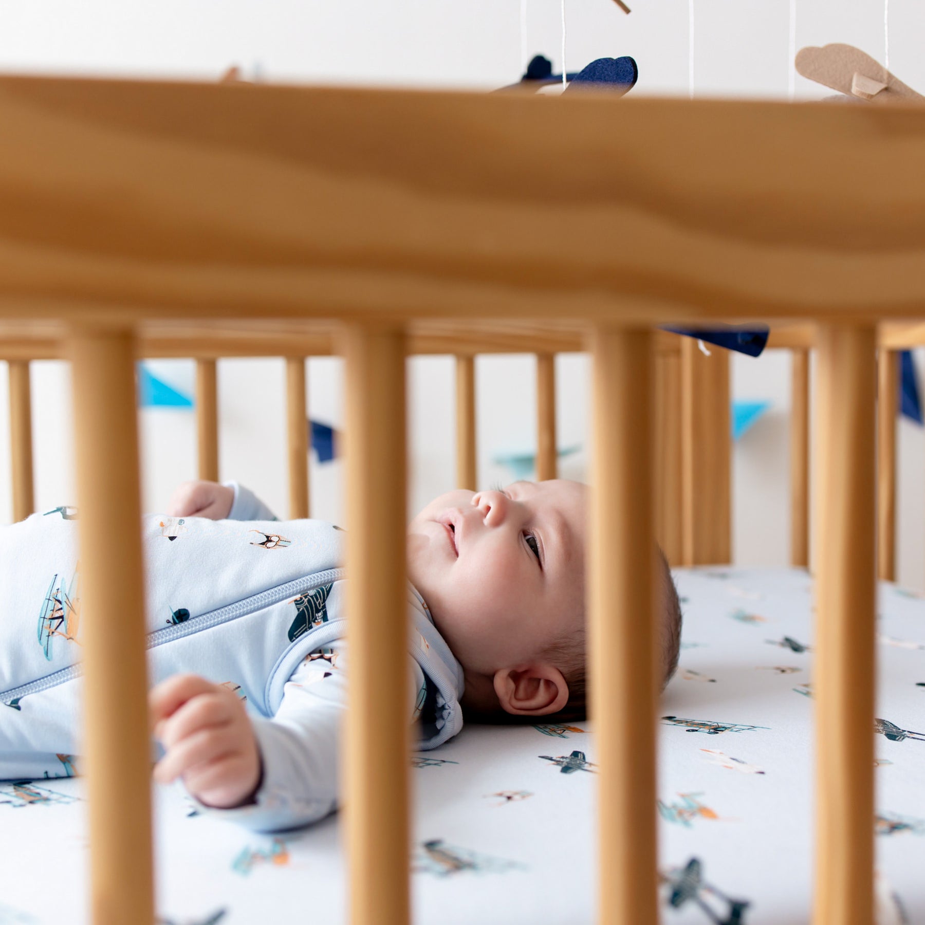 Close up of the crib and the Crib Sheet in Take Off with infant laying in the crib