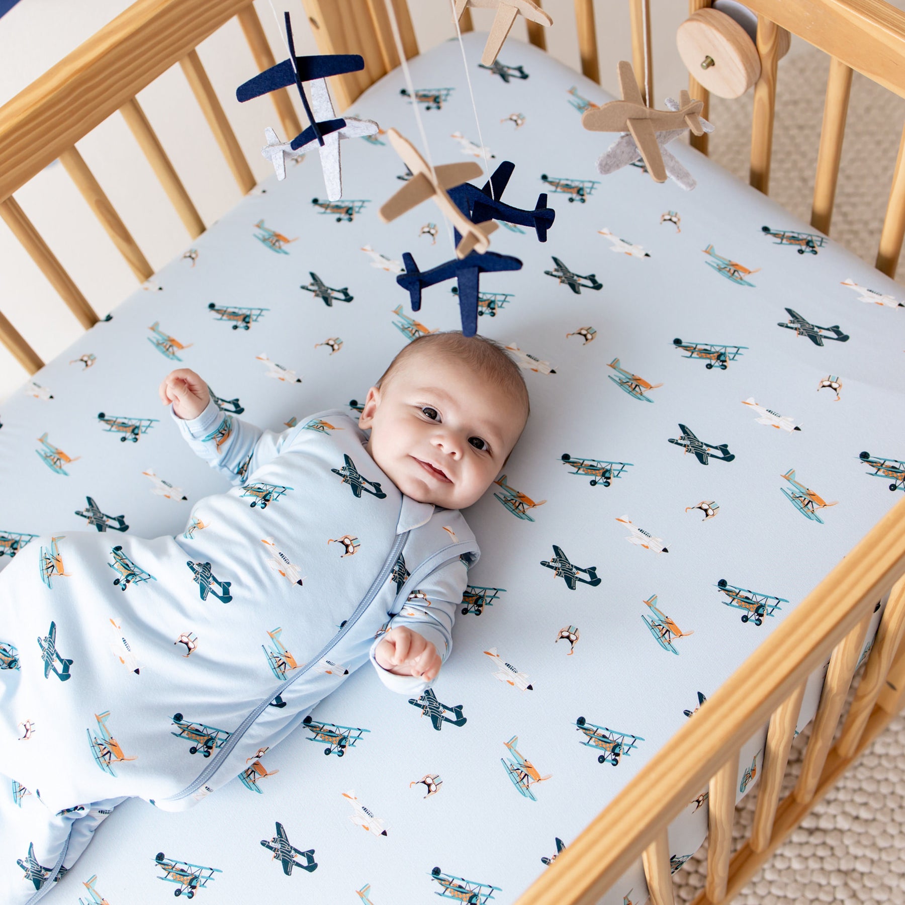 Infant laying in a crib on a Crib Sheet in Take Off wearing a matching sleep bag