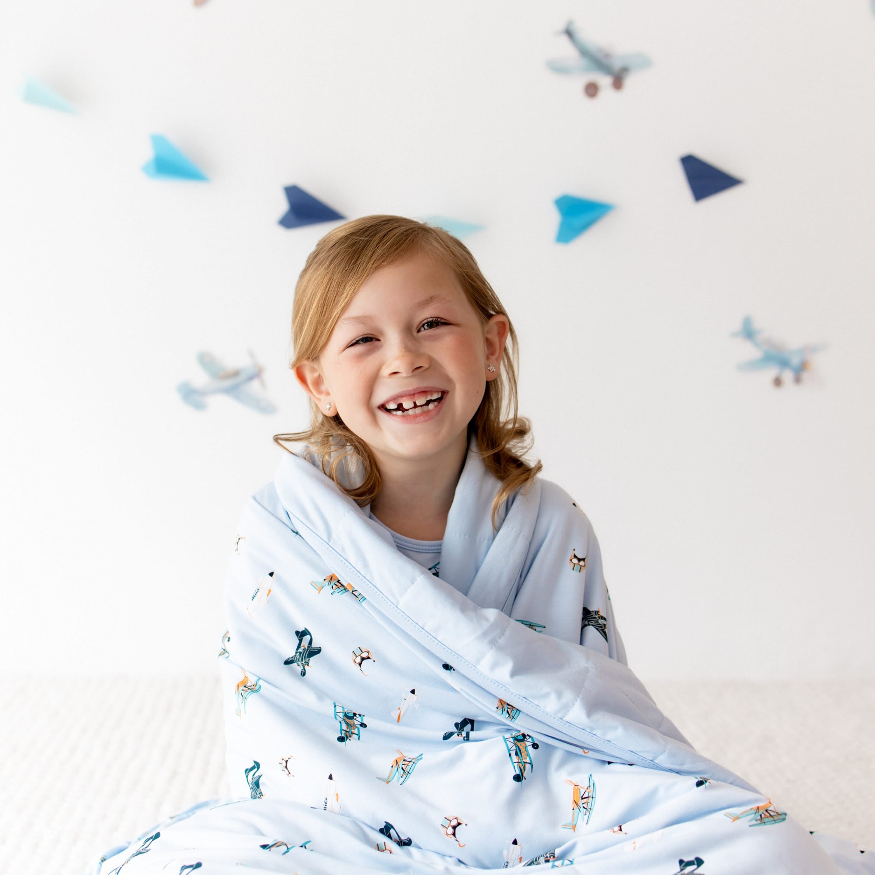 Close up of smiling girl sitting on the floor with he Youth Blanket in Take Off 1.0 wrapped around her