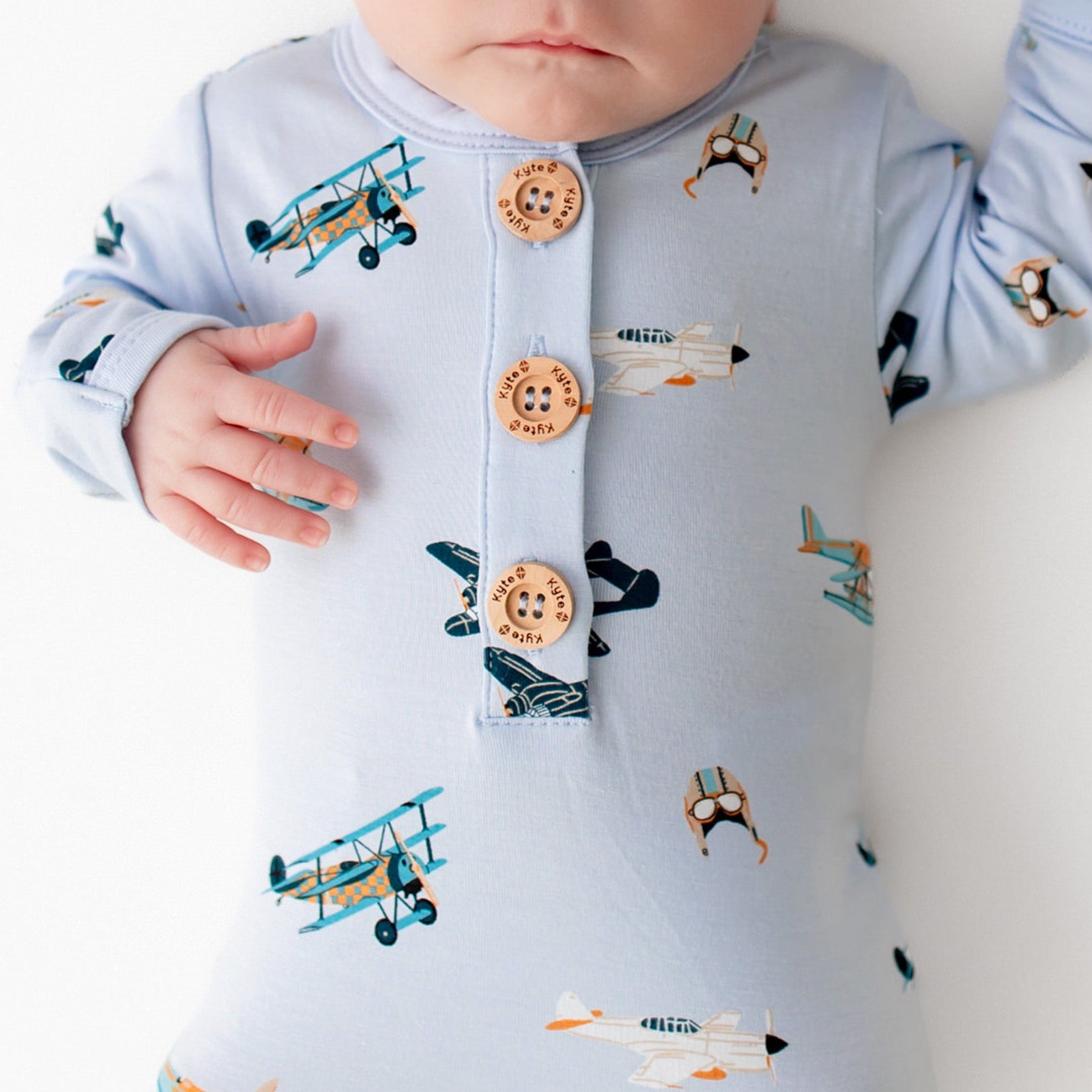 Close up of sleeping newborn wearing the Knotted Gown with Hat Set in Take Off with the Kyte Baby logo wooden buttons visible