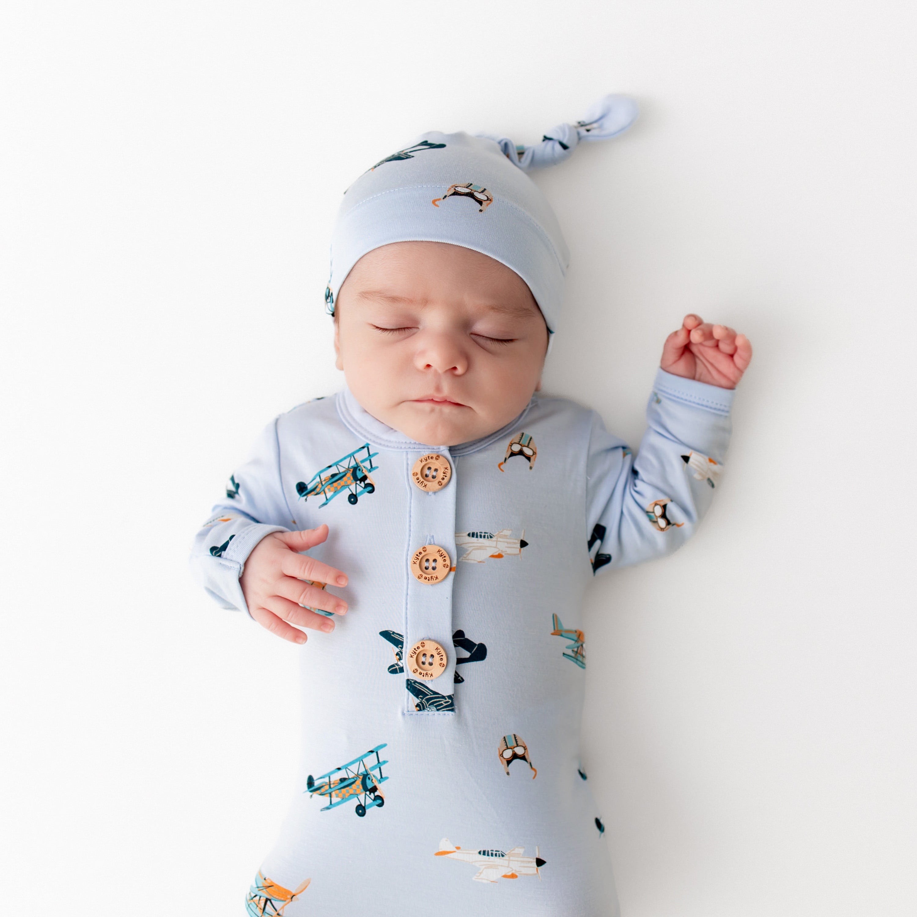 Close up of sleeping newborn wearing the Knotted Gown with Hat Set in Take Off with the Kyte Baby logo wooden buttons visible