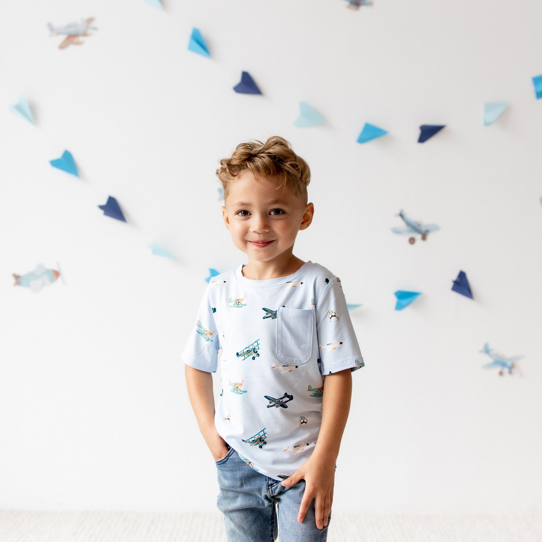 Young boy standing wearing the Toddler Crew Neck Tee in Take Off with light wash jeans